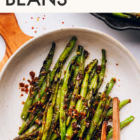 Chopsticks reaching in to pick up spicy stir fried green beans from a bowl