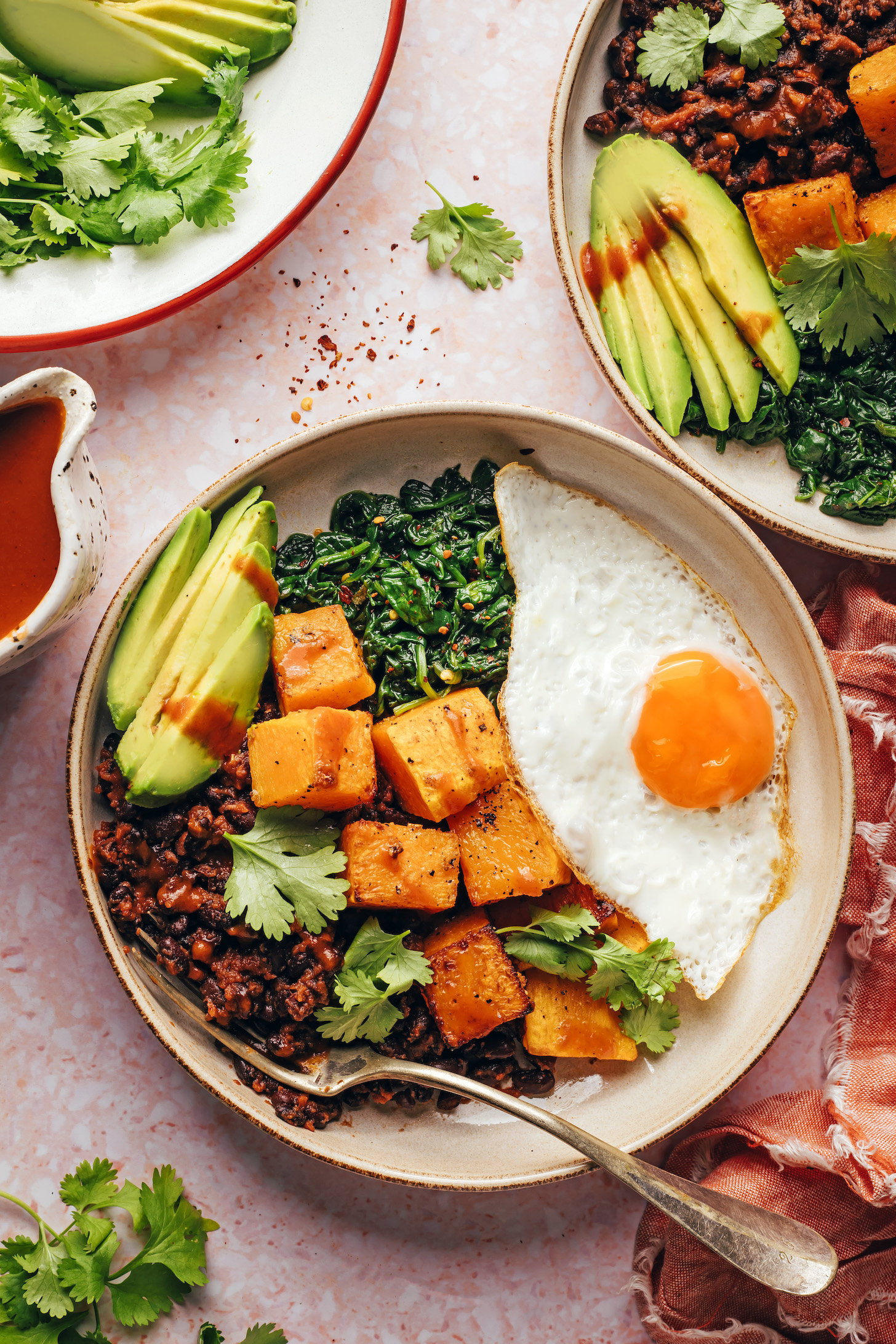 Breakfast bowls with fried eggs, sautéed spinach, roasted squash, avocado, cilantro, and enchilada sauce