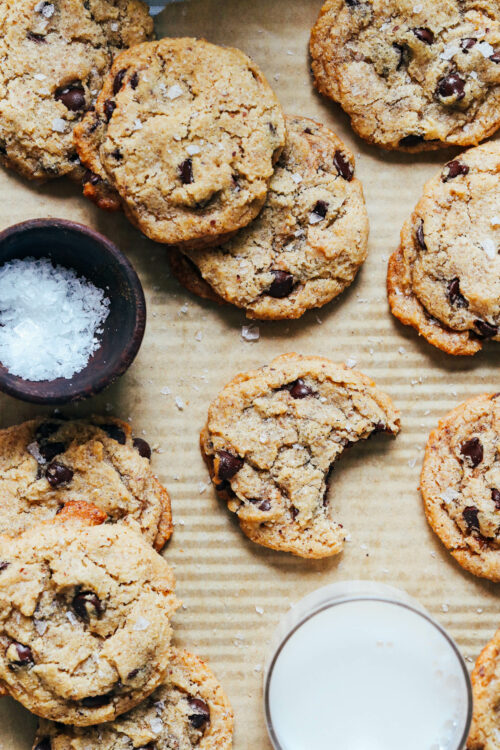Vegan gluten-free chocolate chips on a baking sheet next to flaky salt and dairy-free milk