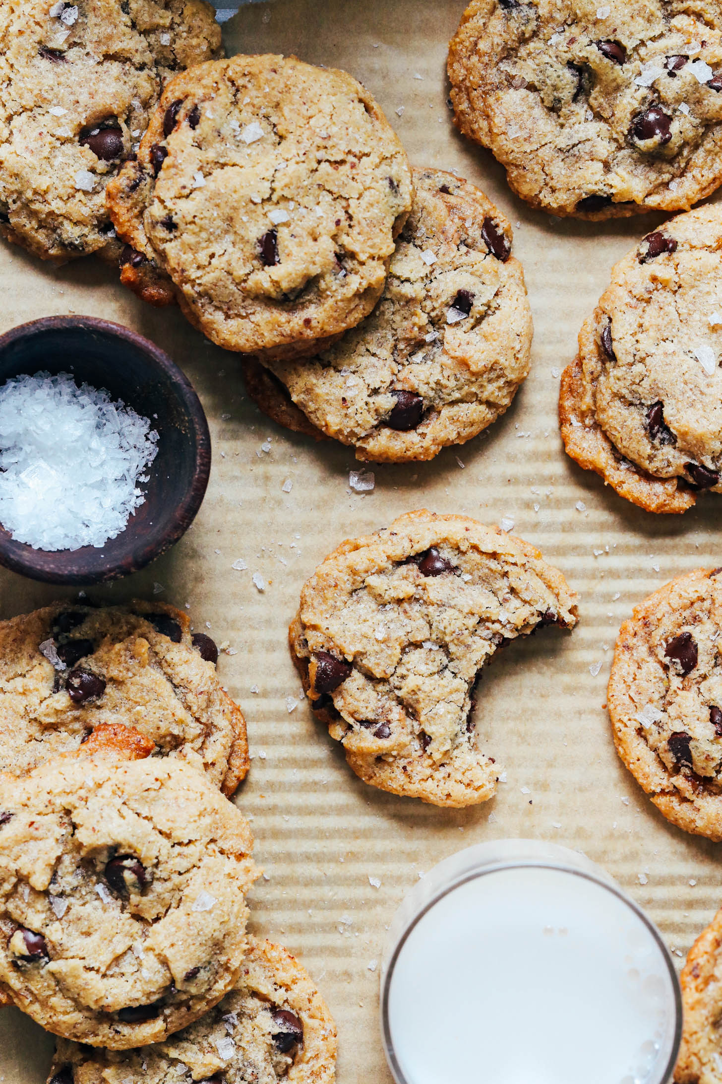 Vegan gluten-free chocolate chips on a baking sheet next to flaky salt and dairy-free milk