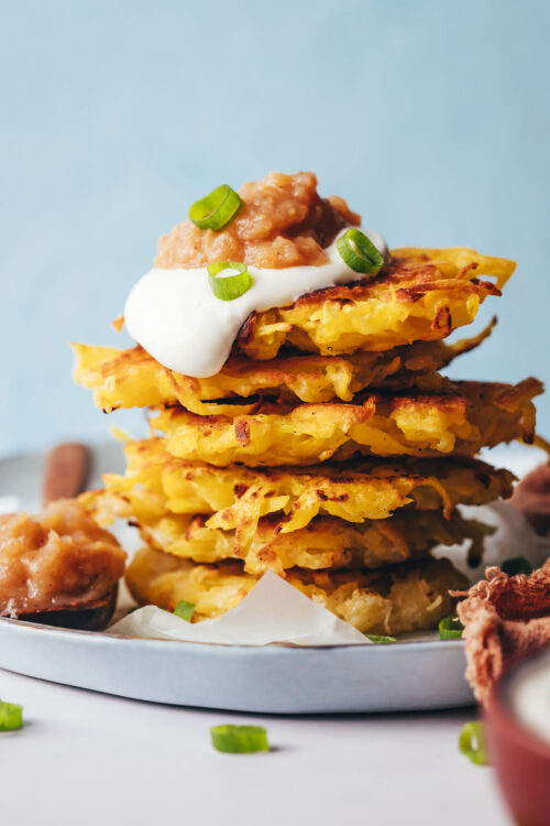 Stack of vegan gluten-free latkes topped with dairy-free sour cream, applesauce, and green onion