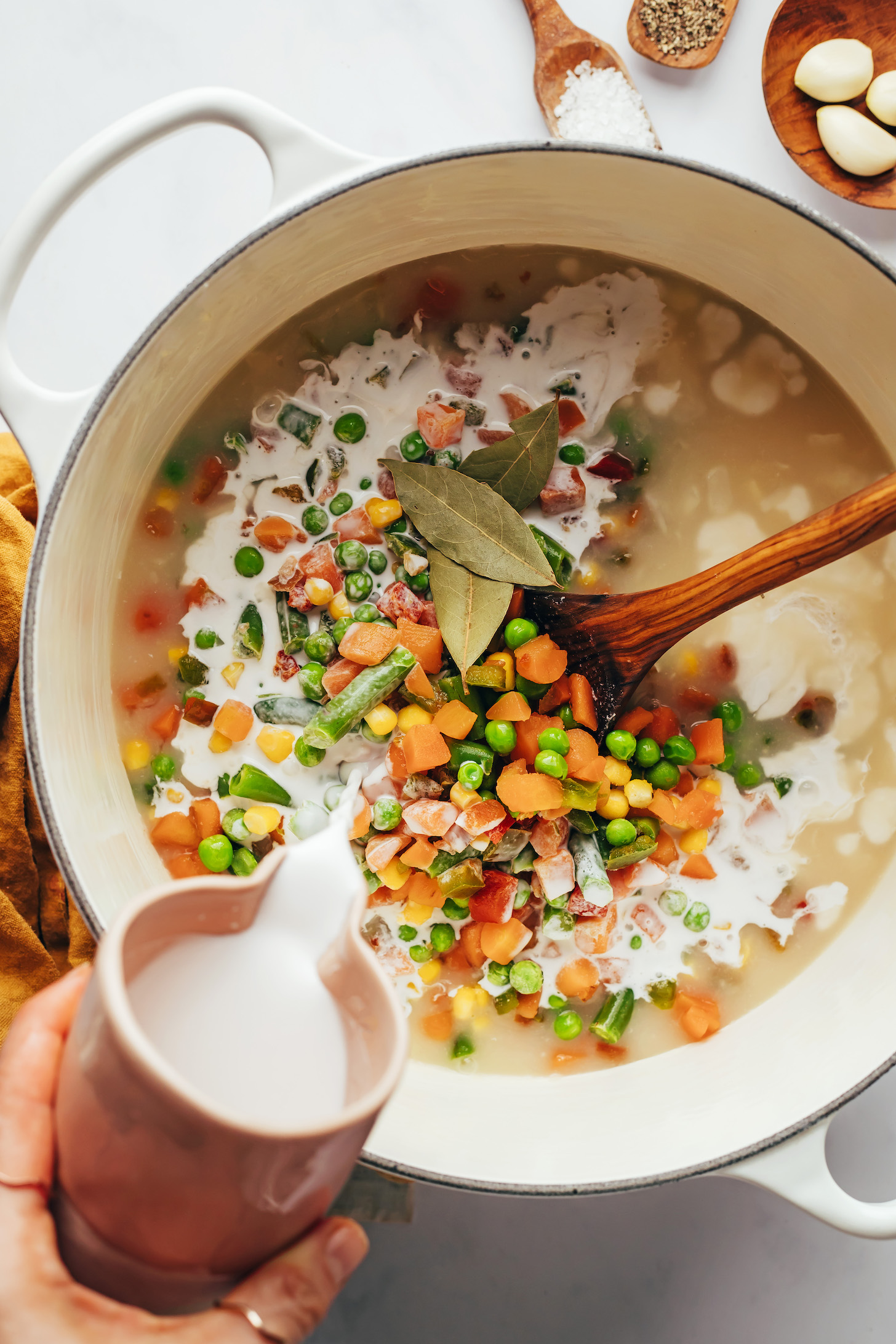 Pouring coconut milk over frozen mixed vegetables in a pot of soup