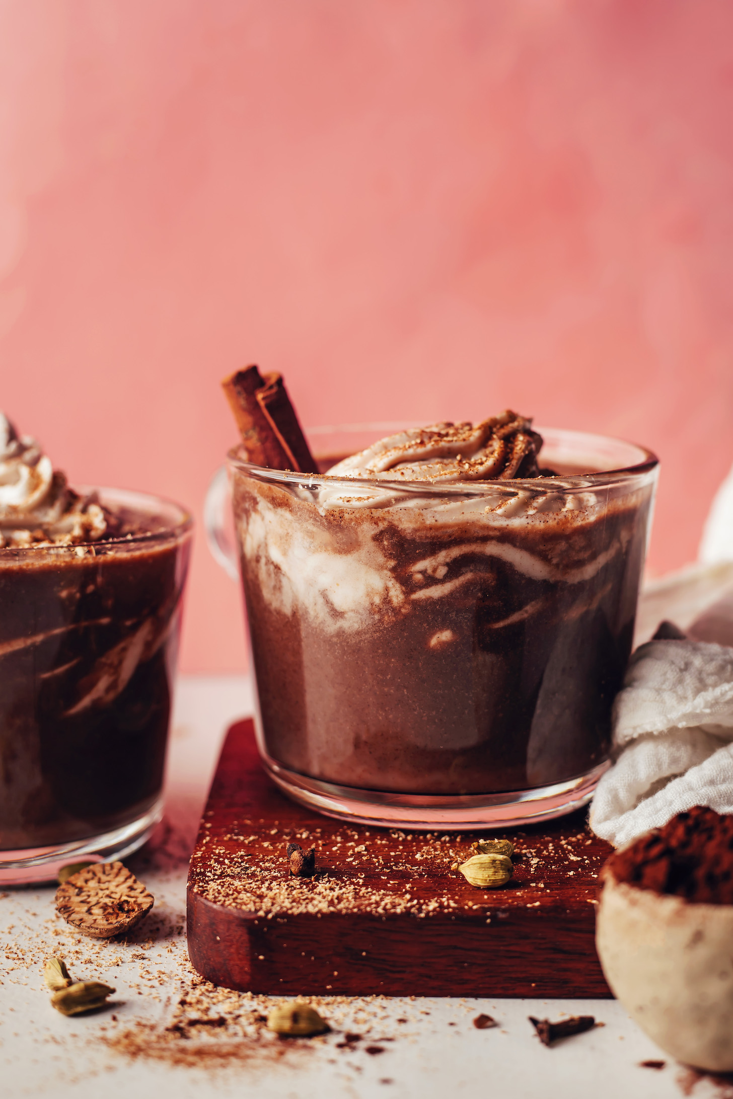 Side view of two mugs of dairy-free hot chocolate topped with coconut whipped cream and chai spices