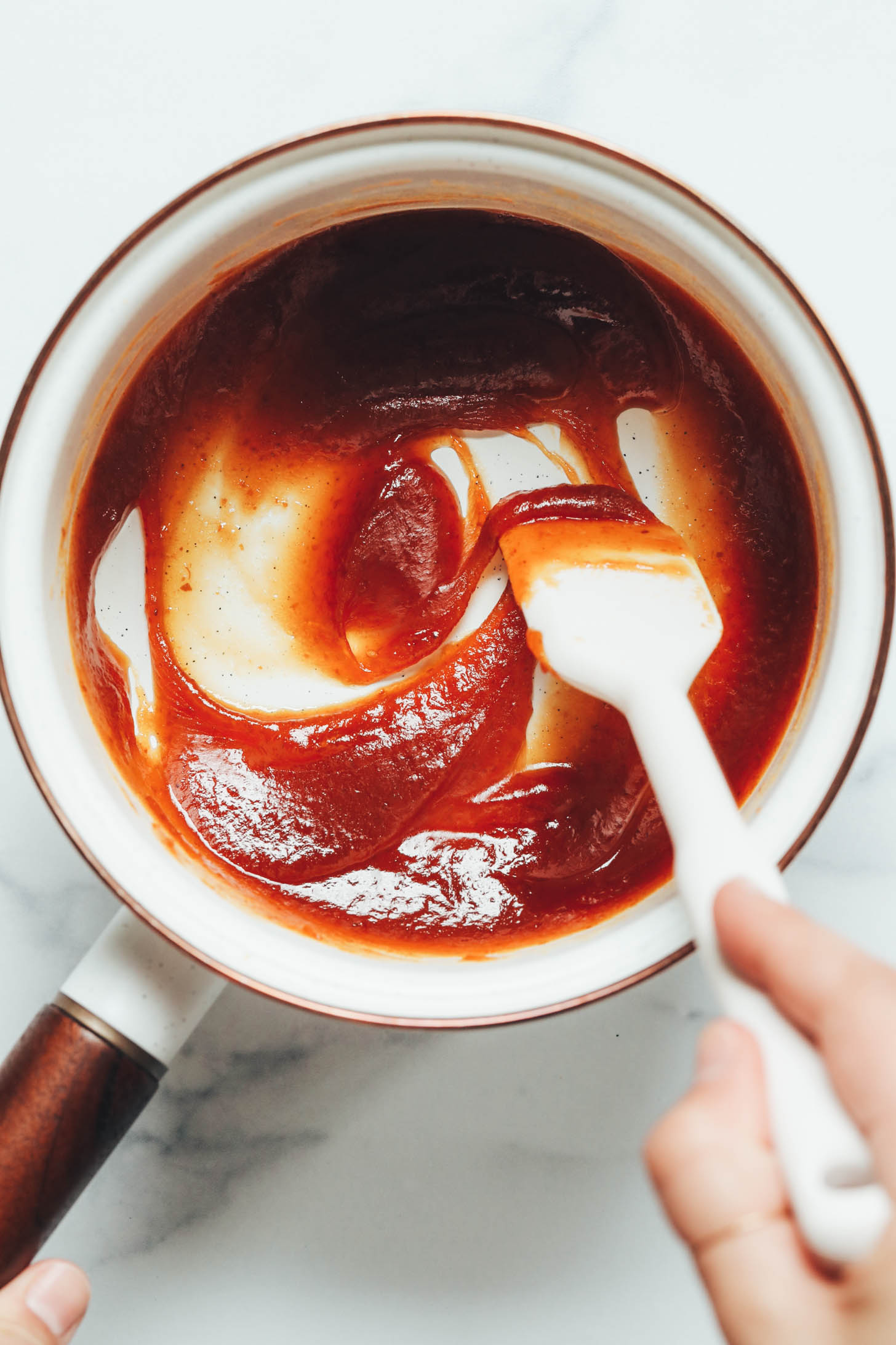 Using a rubber spatula to stir together a thick maple syrup and pumpkin mixture in a saucepan