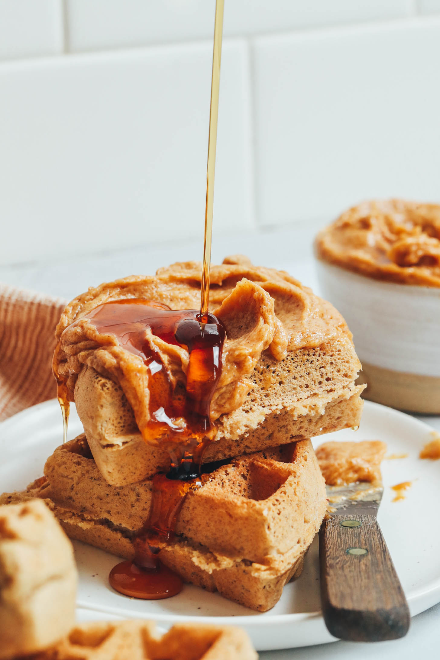 Drizzling maple syrup onto a stack of waffles