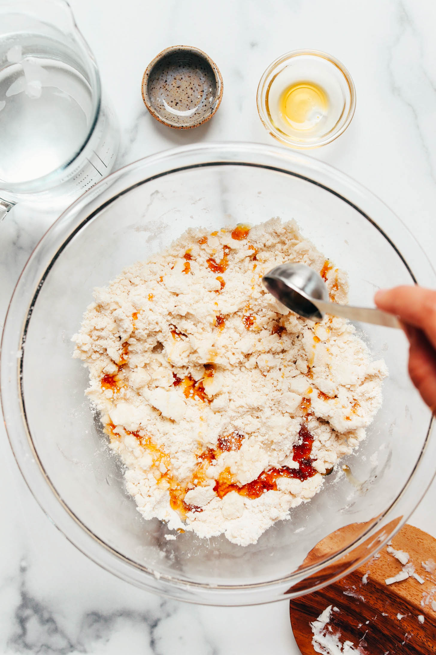 Using a tablespoon to pour maple syrup into a bowl of dry ingredients