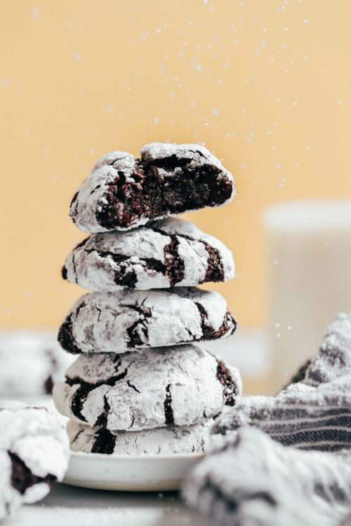 Sprinkling powdered sugar on a stack of gluten-free chocolate crinkle cookies