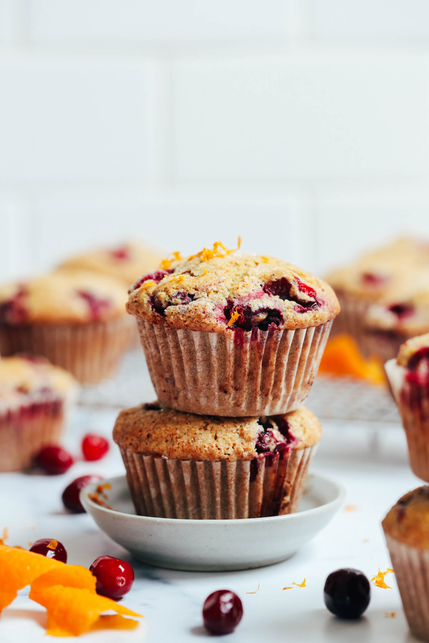 Orange zest sprinkled over a stack of vegan gluten-free cranberry orange muffins