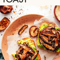 Slices of mushroom avocado toast on a plate next to vegan parmesan and red pepper flakes