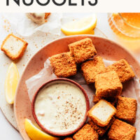 Hand reaching in to pick up a tofu nugget from a plate