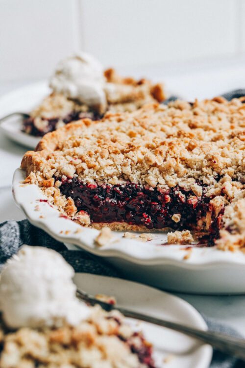 Slice of mixed berry pie next to a pie pan with the rest of it