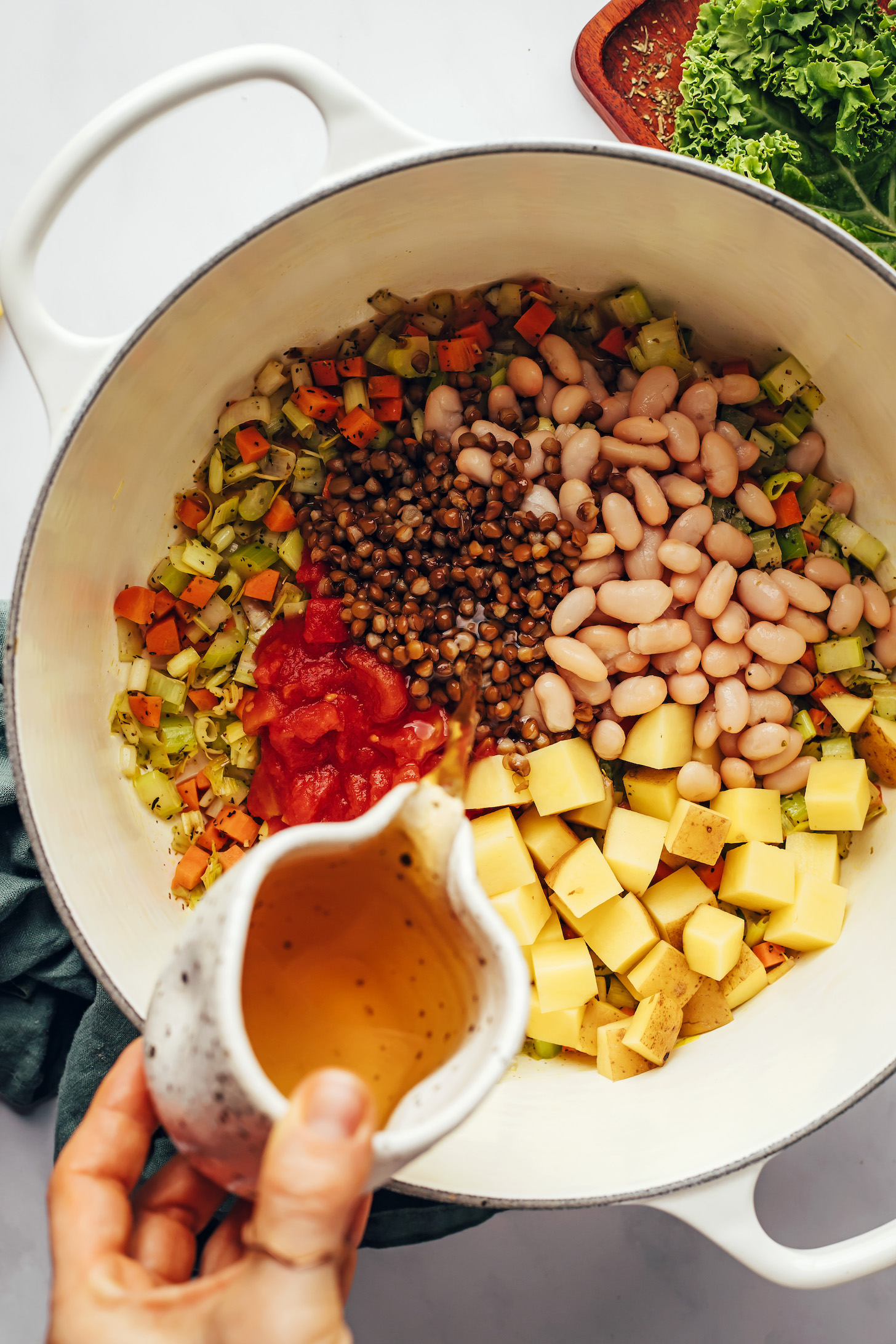 Pouring vegetable broth over lentils in a Dutch oven
