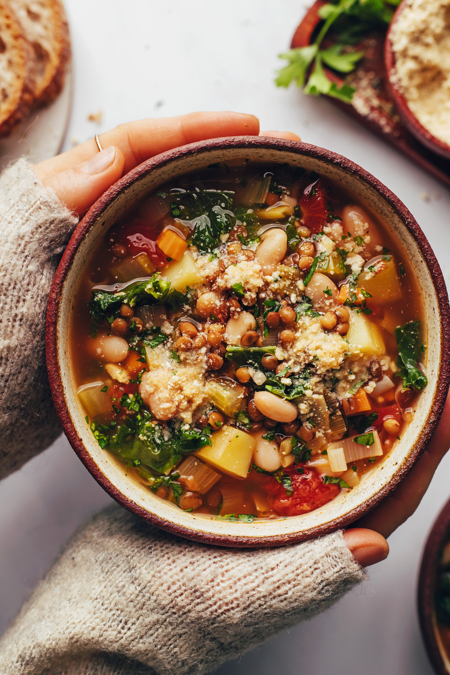 Hands holding a bowl of lentil, white bean, and vegetable soup