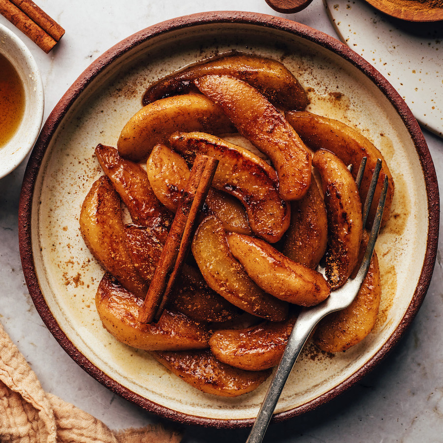 Cinnamon stick over a plate of caramelized cinnamon-spiced pears