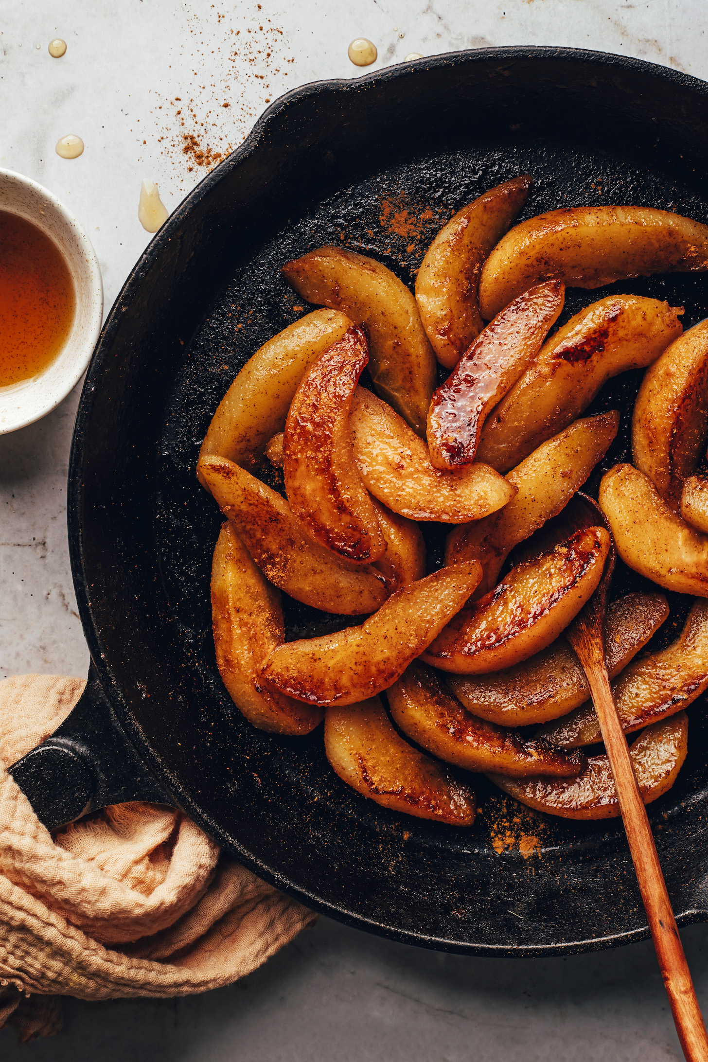 Wooden spoon in a skillet of caramelized sliced cinnamon pears