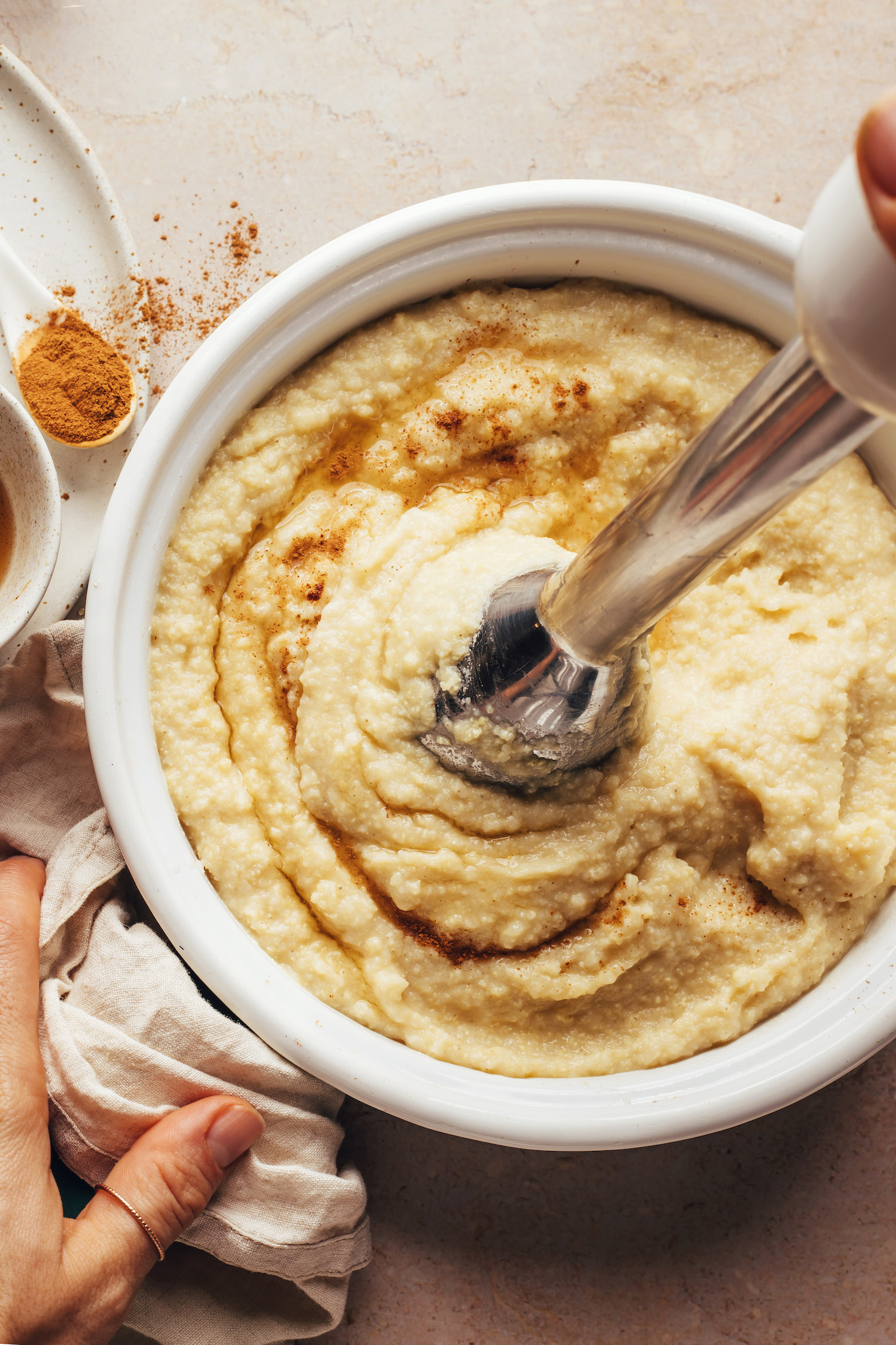 Using an immersion blender to purée cooked millet into a porridge