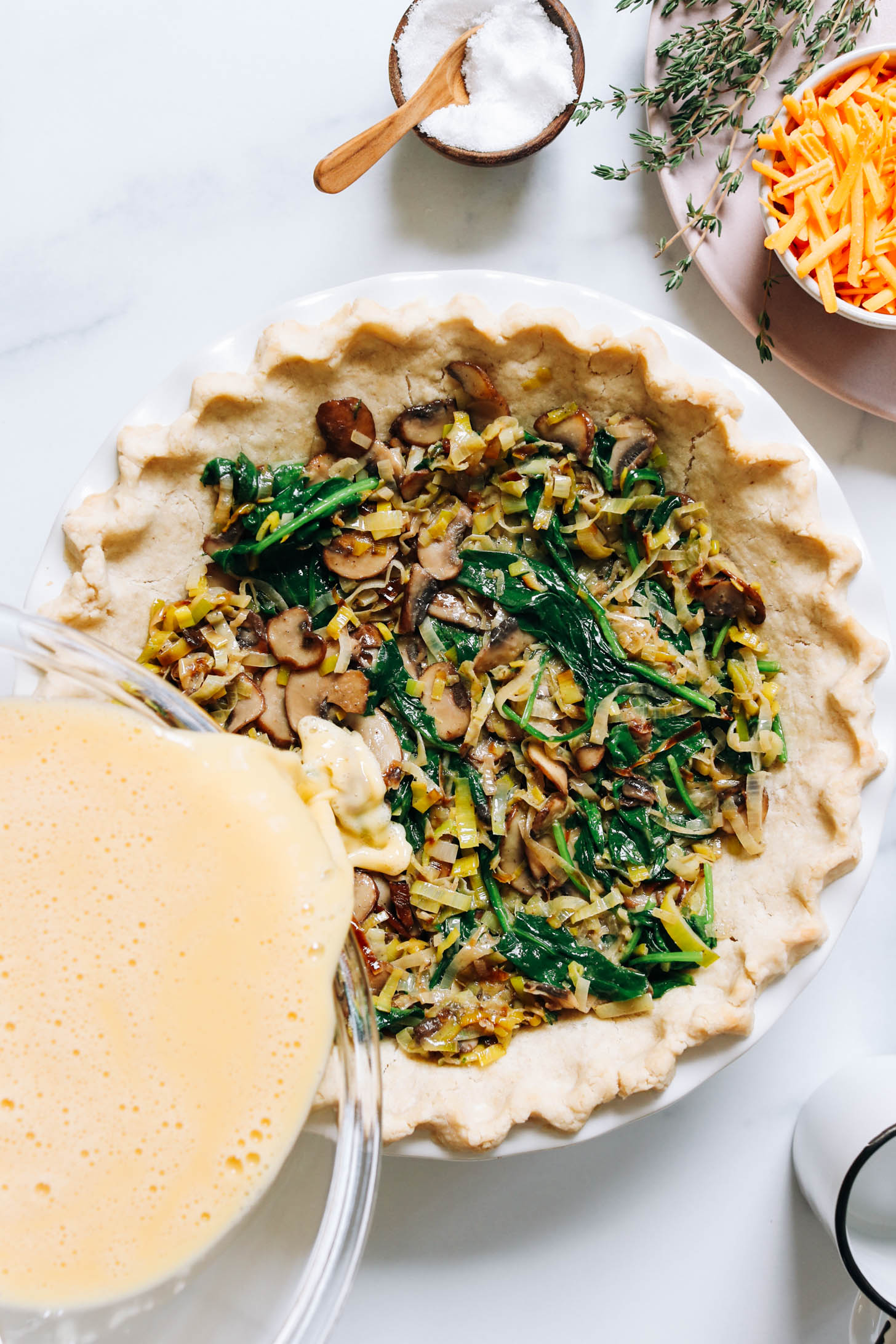 Pouring an egg mixture over sautéed leeks, spinach, and mushrooms