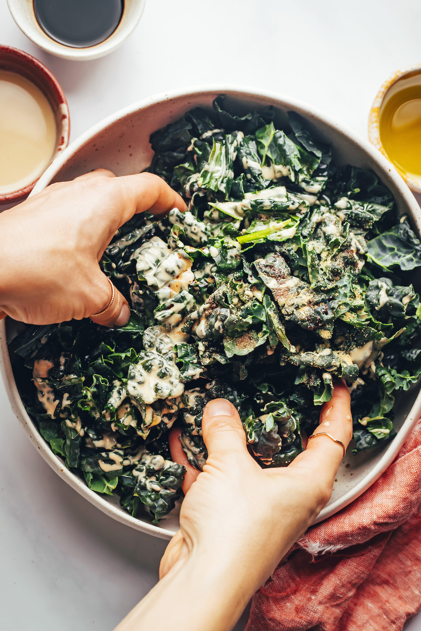 Massaging kale with balsamic vinegar, olive oil, tahini, salt, pepper, and garlic powder