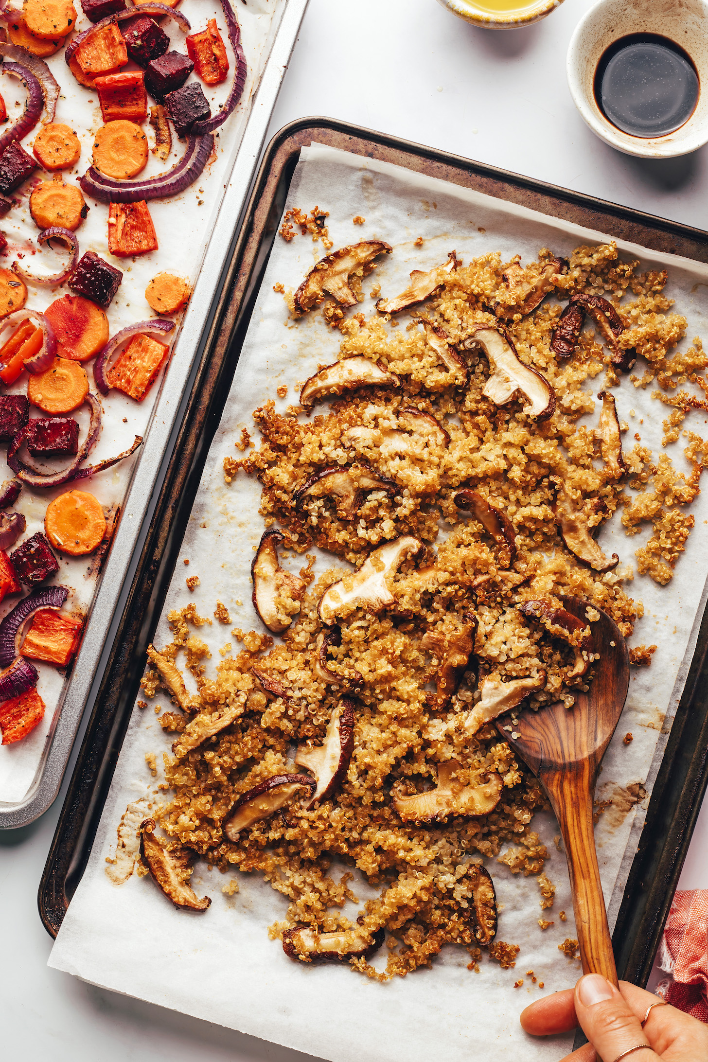 Parchment-lined baking sheets of quinoa, mushrooms, and root veggies