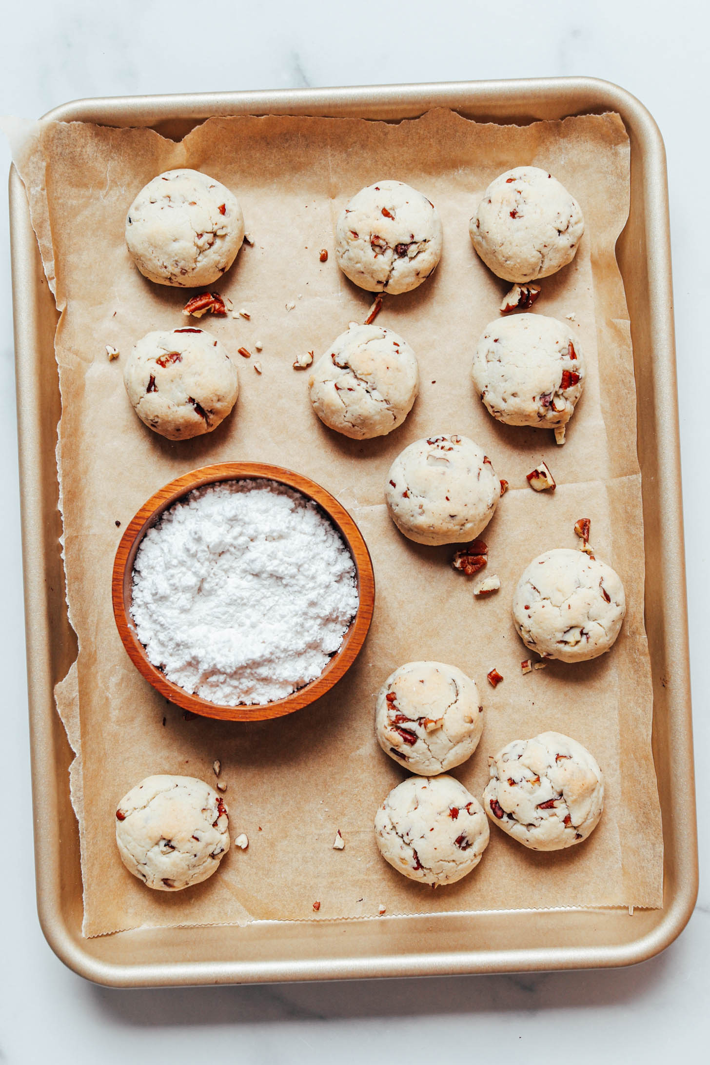 Bowl of powdered sugar and freshly baked pecan cookies on a baking sheet