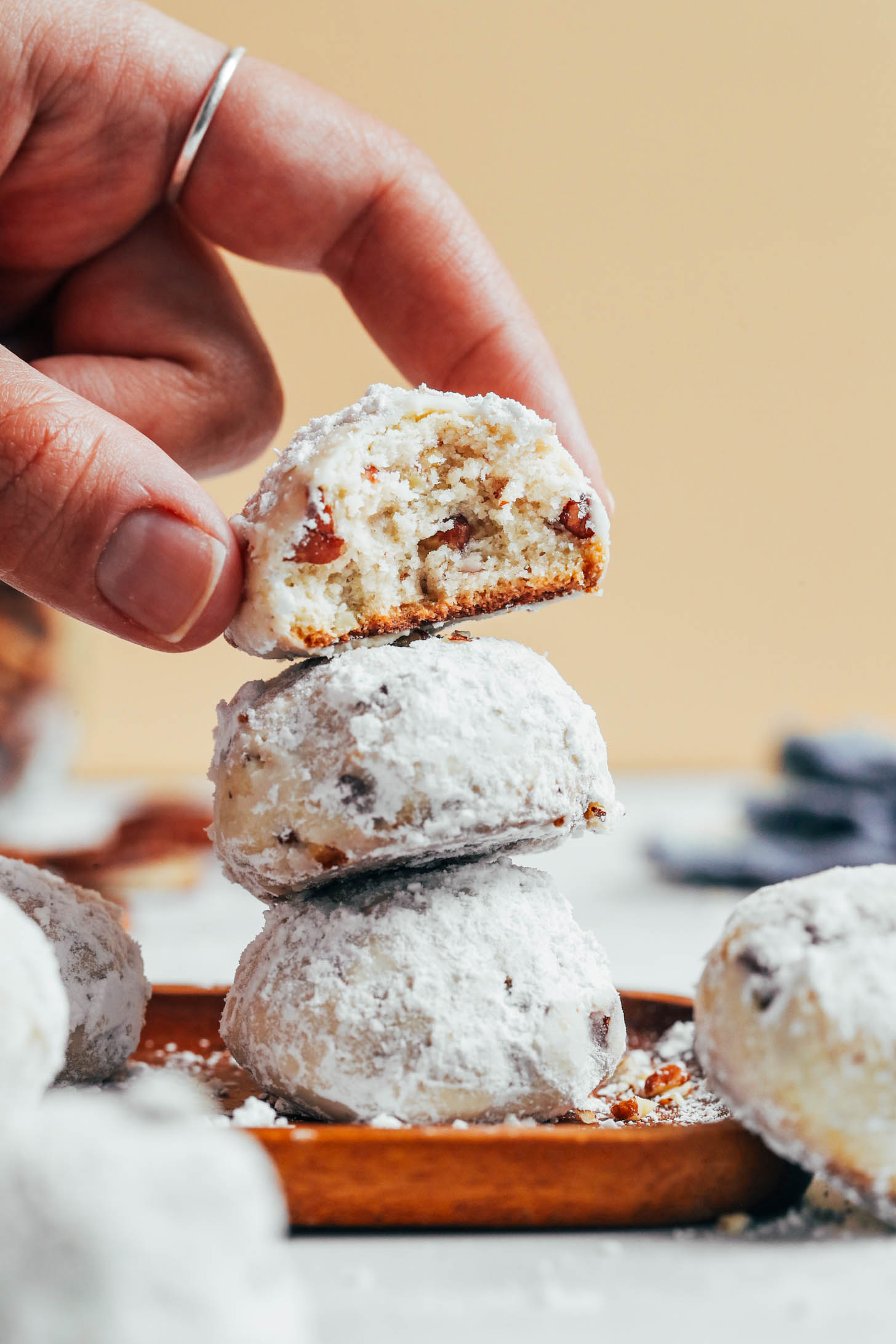 Holding a partially eaten vegan and gluten-free Mexican wedding cookie to show the inner crispy texture