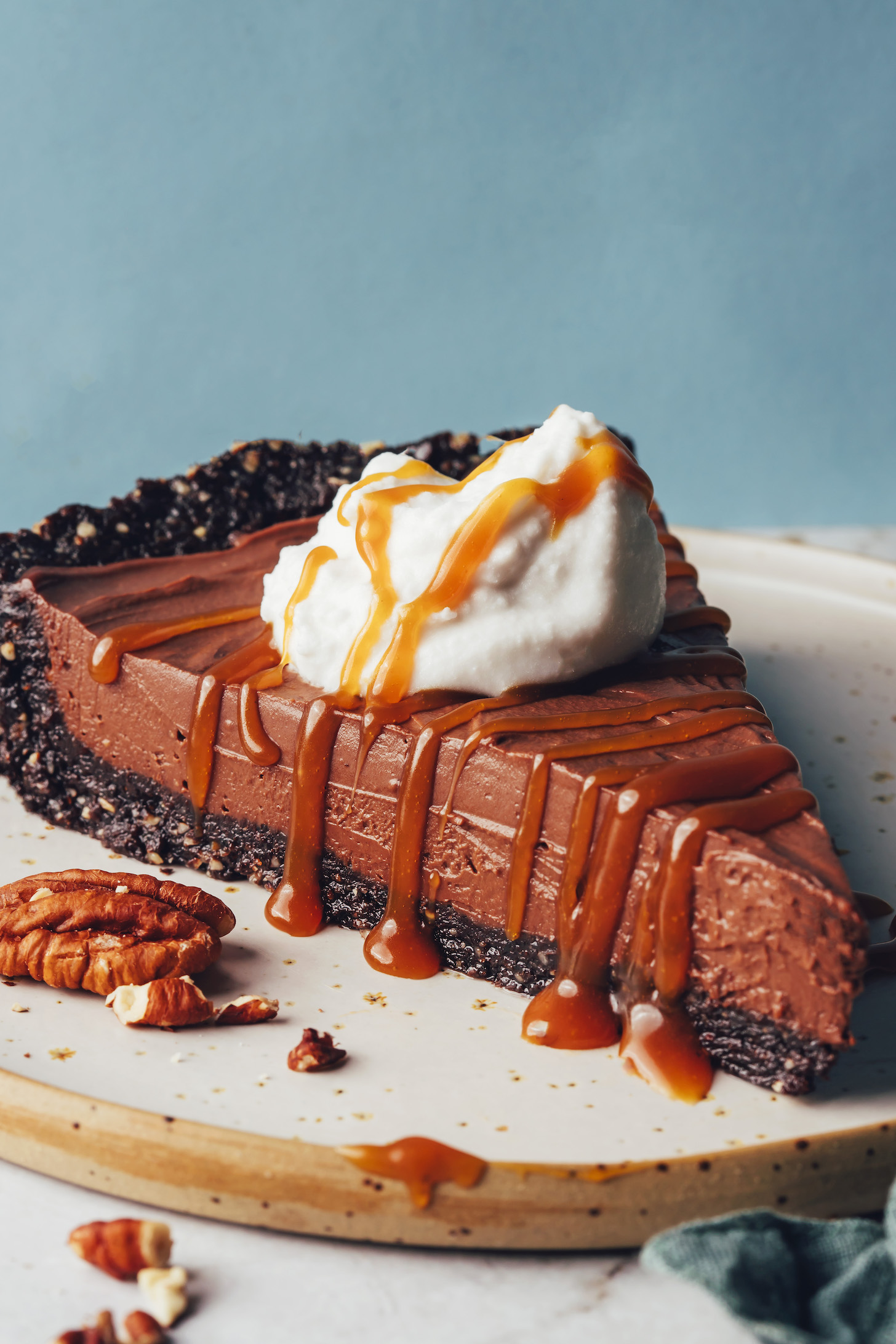 Pecans next to a slice of no-bake double chocolate mousse pie topped with coconut whipped cream and caramel sauce