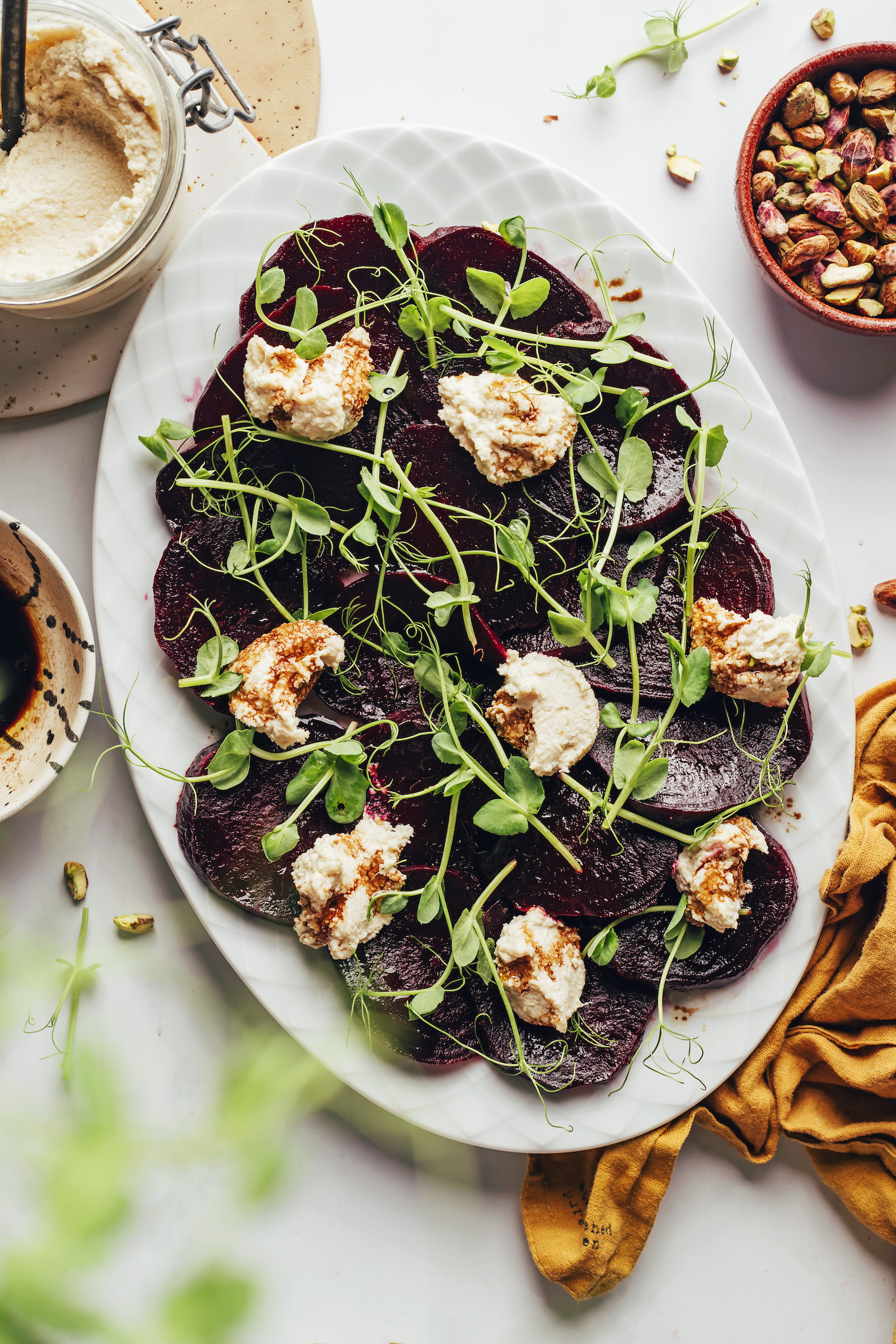 Pistachios, vegan goat cheese, and balsamic dressing next to a platter of roasted beet salad