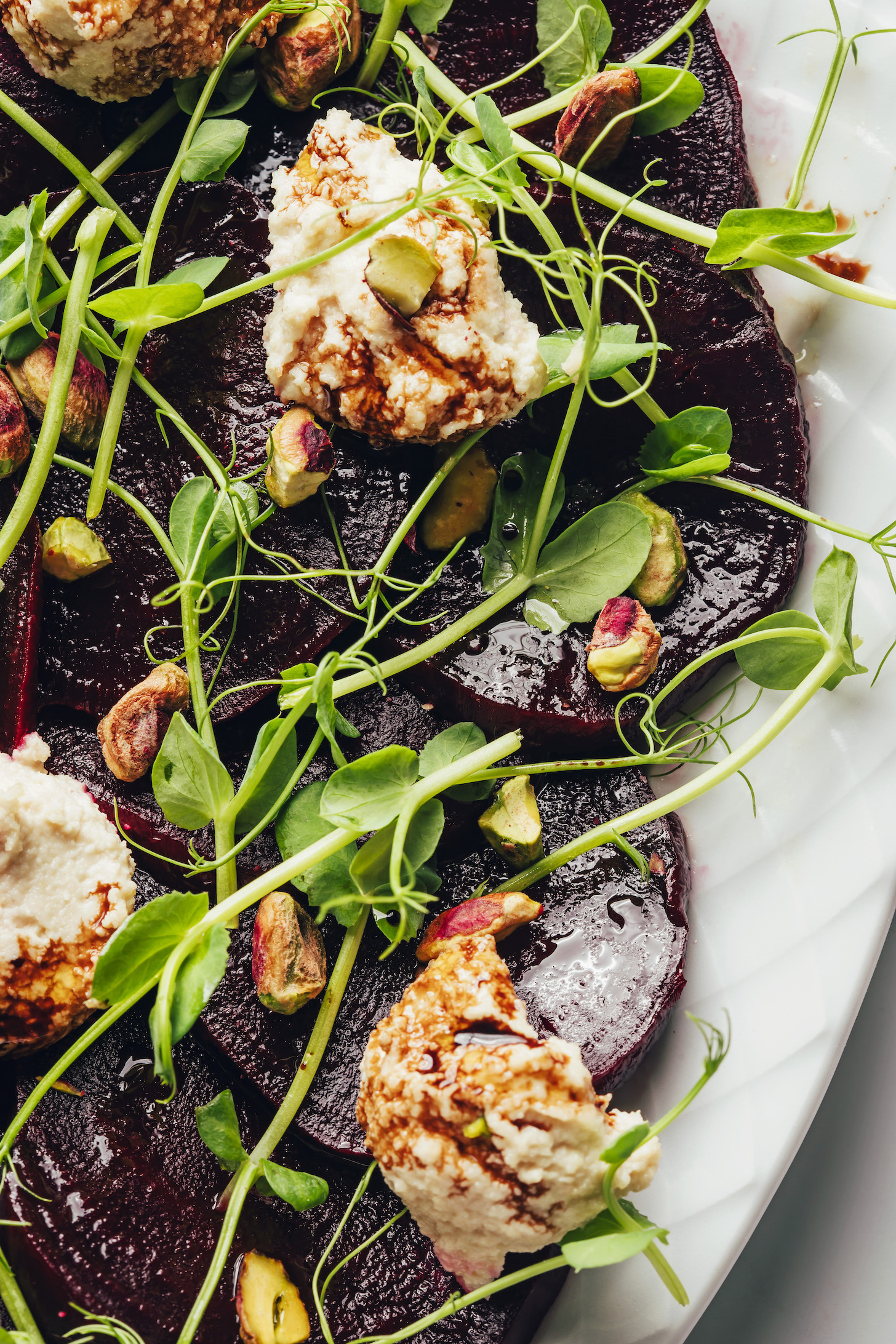 Close up shot of microgreens and spoonfuls of homemade vegan goat cheese on a roasted beet salad