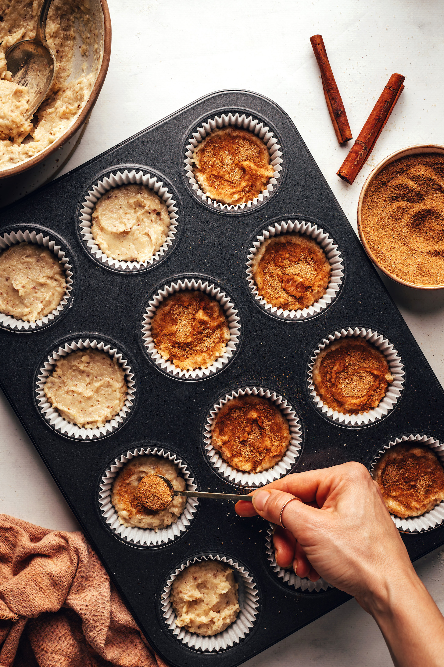 Sprinkling cinnamon sugar into muffin tins of dough