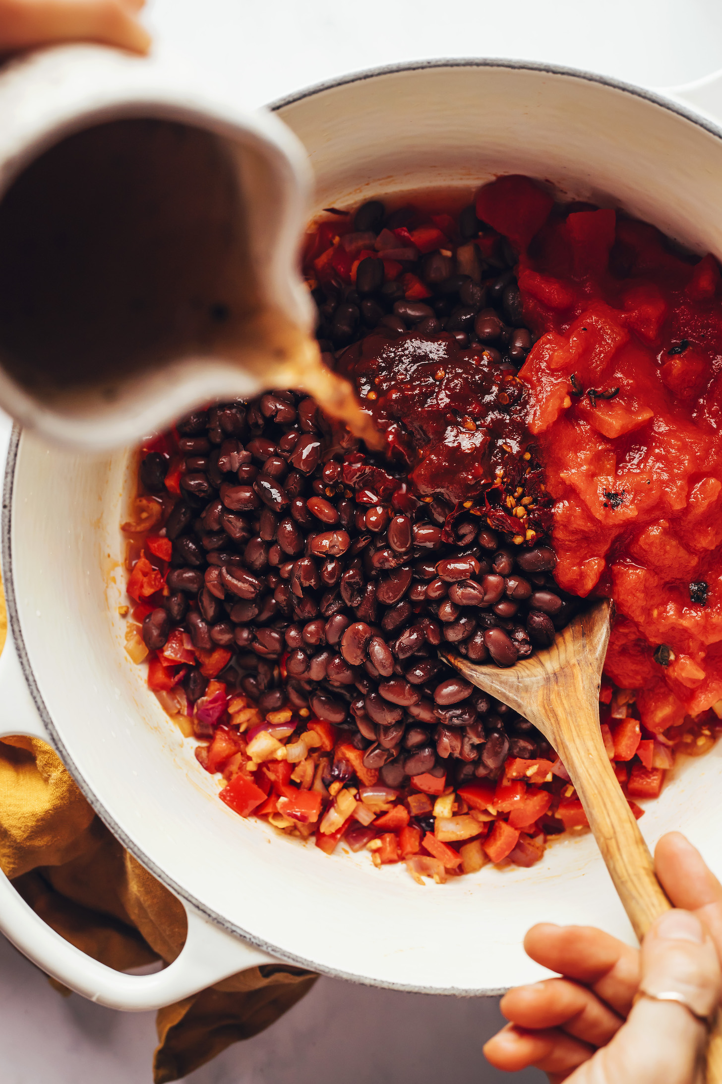 Pouring vegetable broth into a Dutch oven over other ingredients