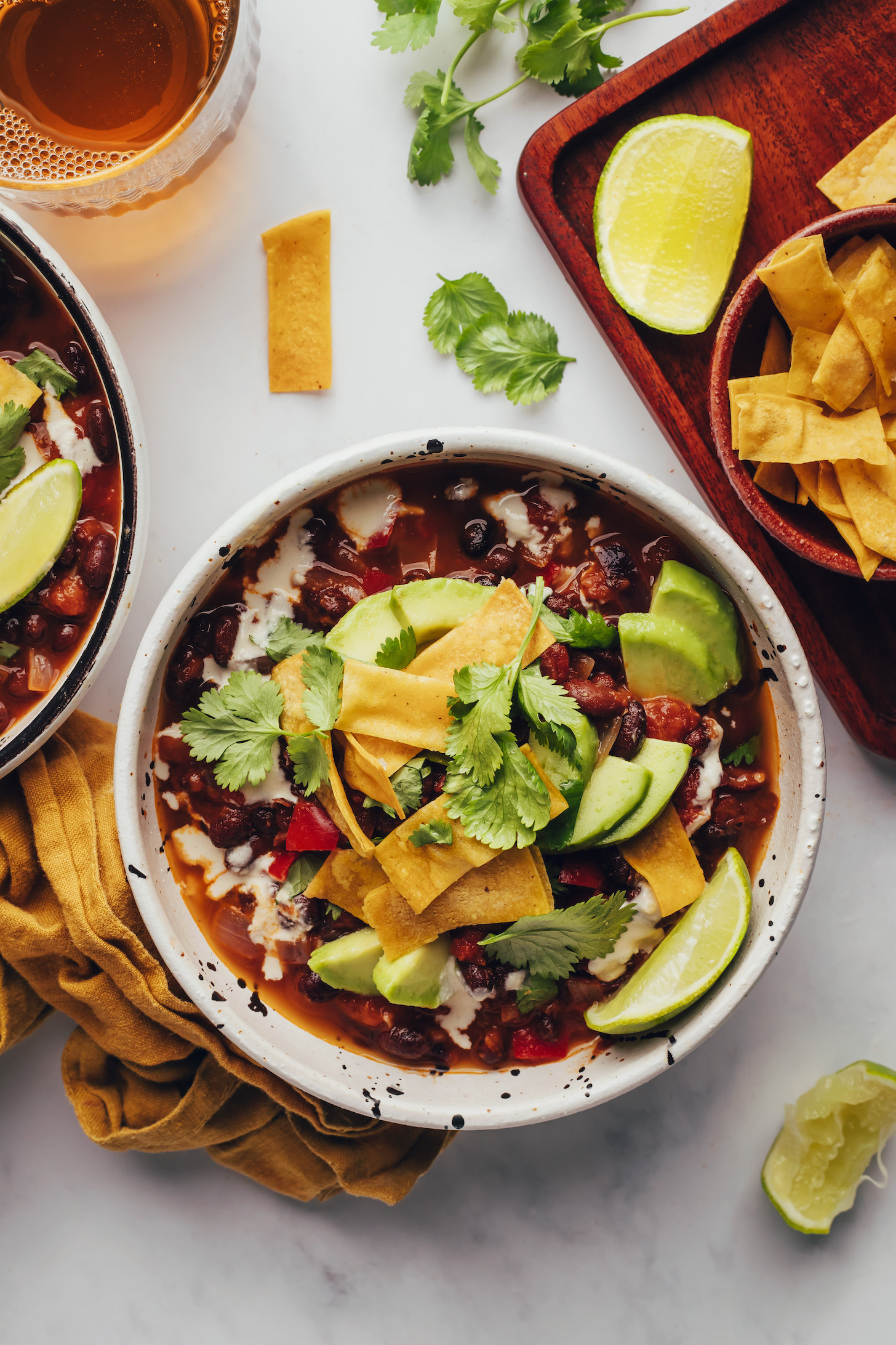 Tortilla strips and lime wedges next to bowls of chipotle black bean soup with toppings