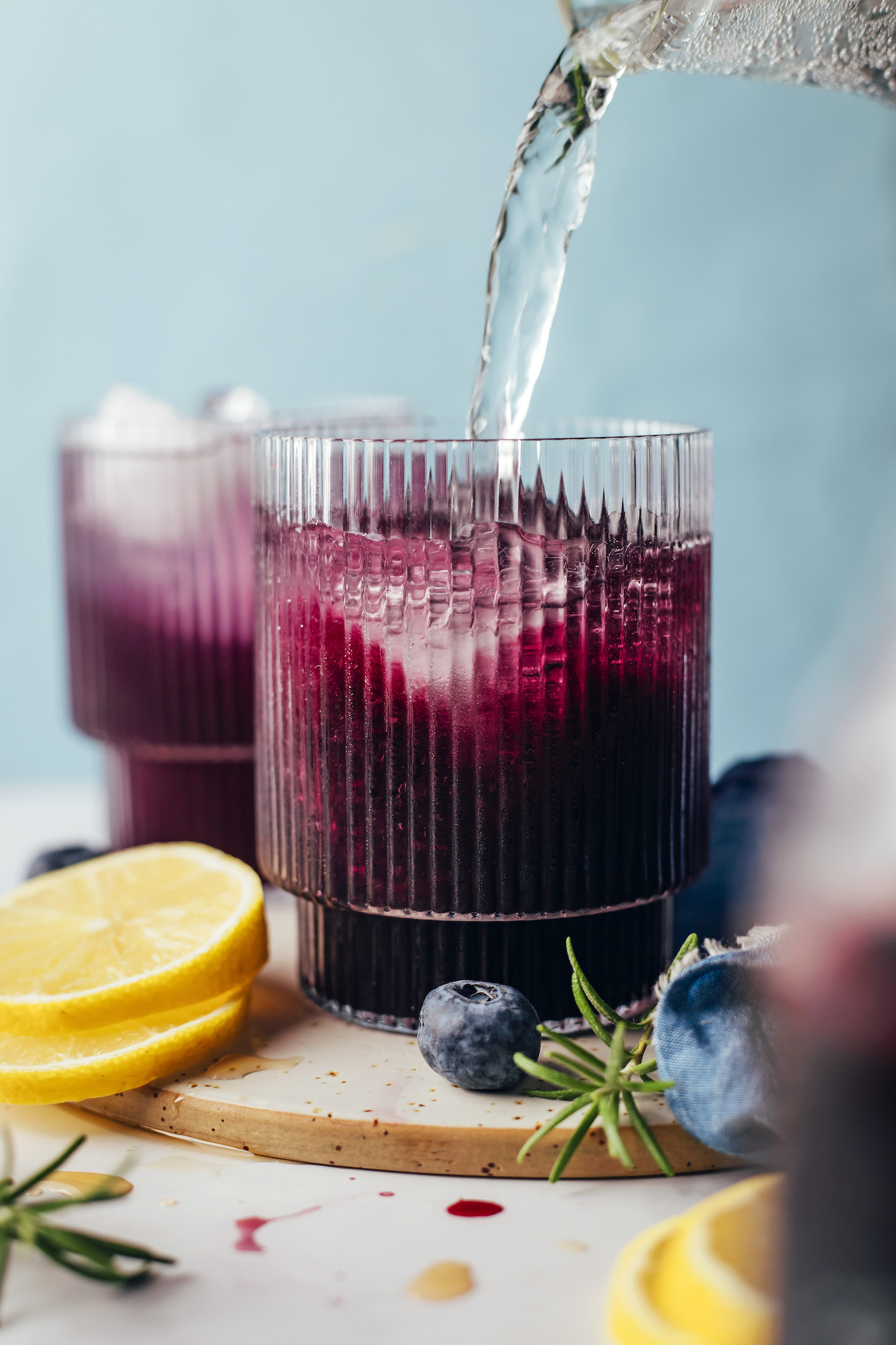 Sparkling water being poured into a glass with ice cubes and naturally sweetened blueberry simple syrup