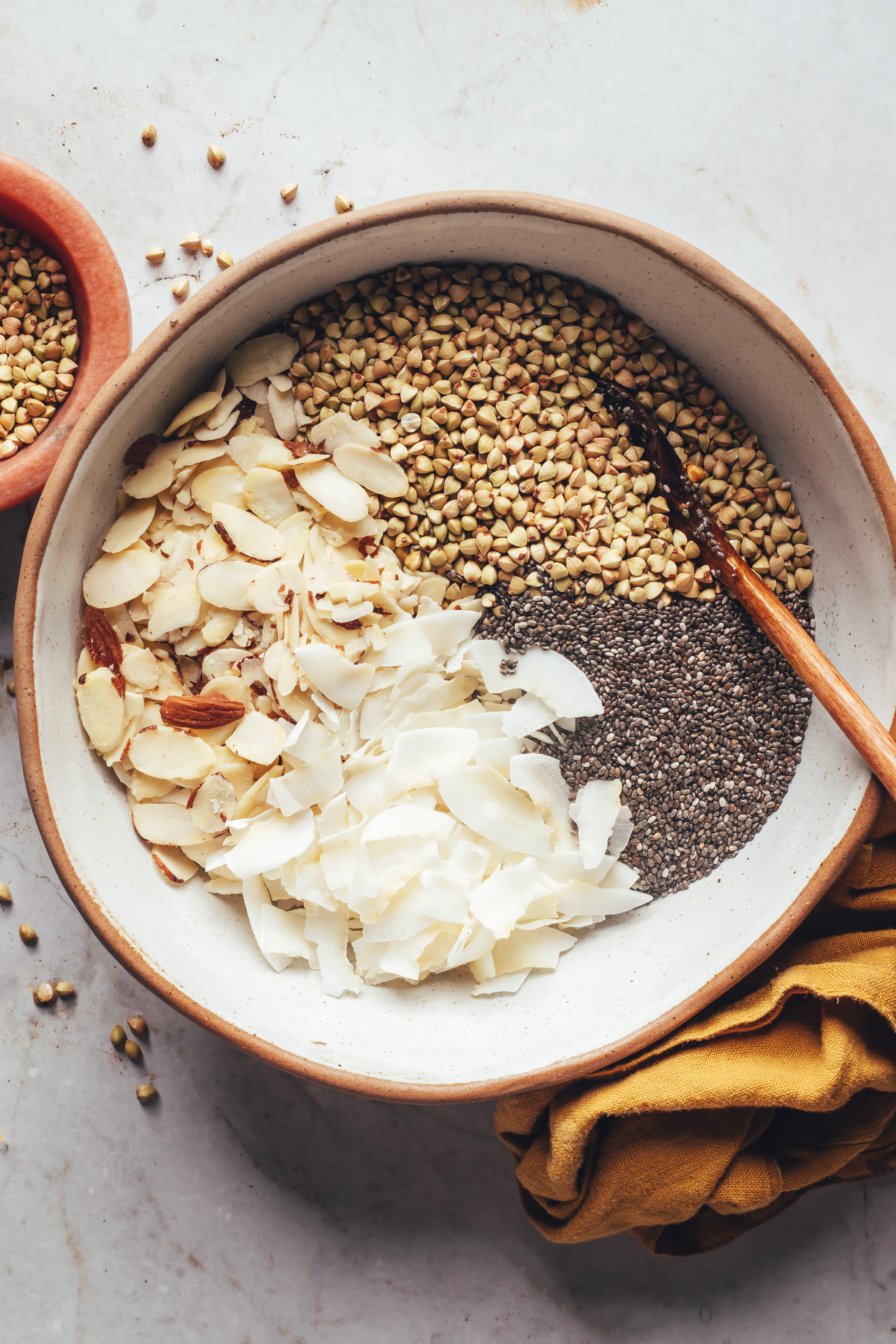 Stirring together buckwheat groats, sliced almonds, coconut flakes, and chia seeds.