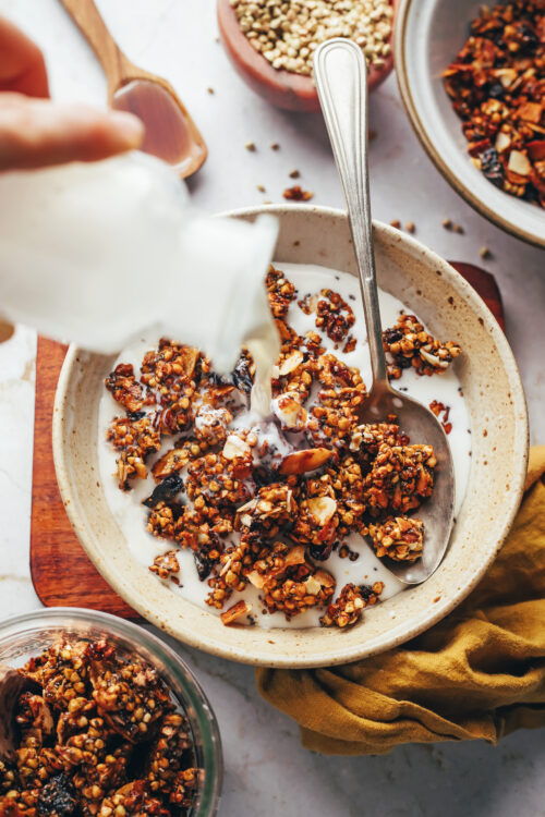 Pouring dairy-free milk into a bowl of buckwheat almond granola