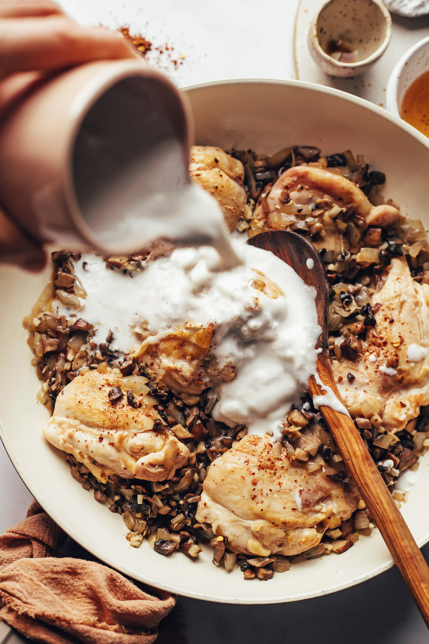 Pouring coconut milk over sautéed mushrooms and browned chicken thighs