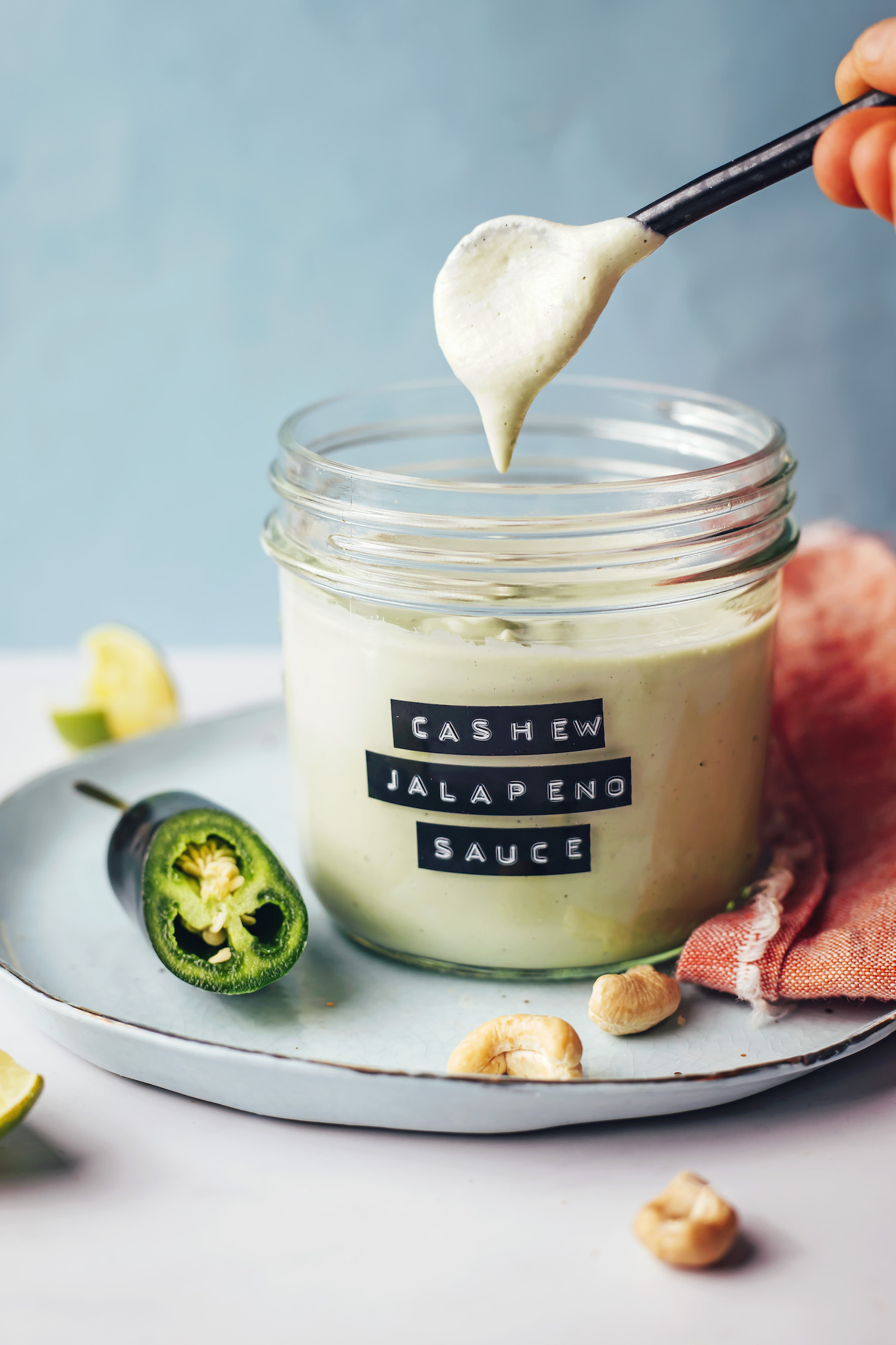 Holding a spoonful of creamy cashew jalapeño sauce over a glass jar