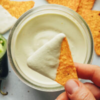 Holding a tortilla chip with sauce on it over a glass jar with more sauce