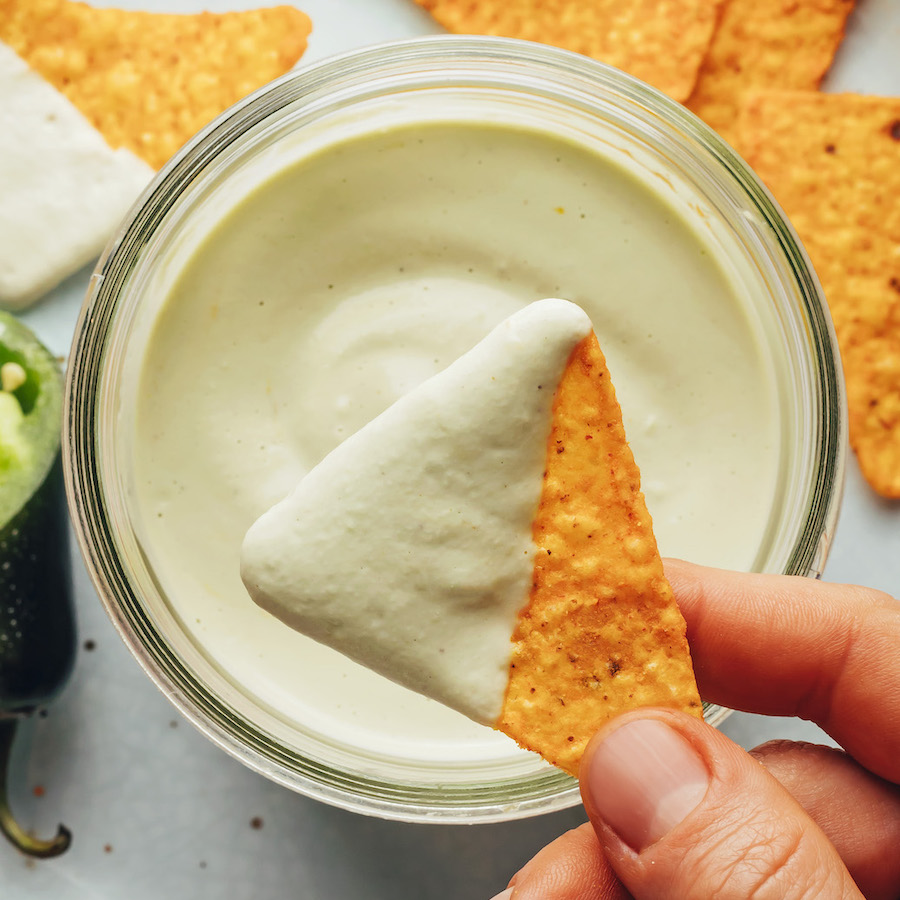 Holding a tortilla chip with sauce on it over a glass jar with more sauce