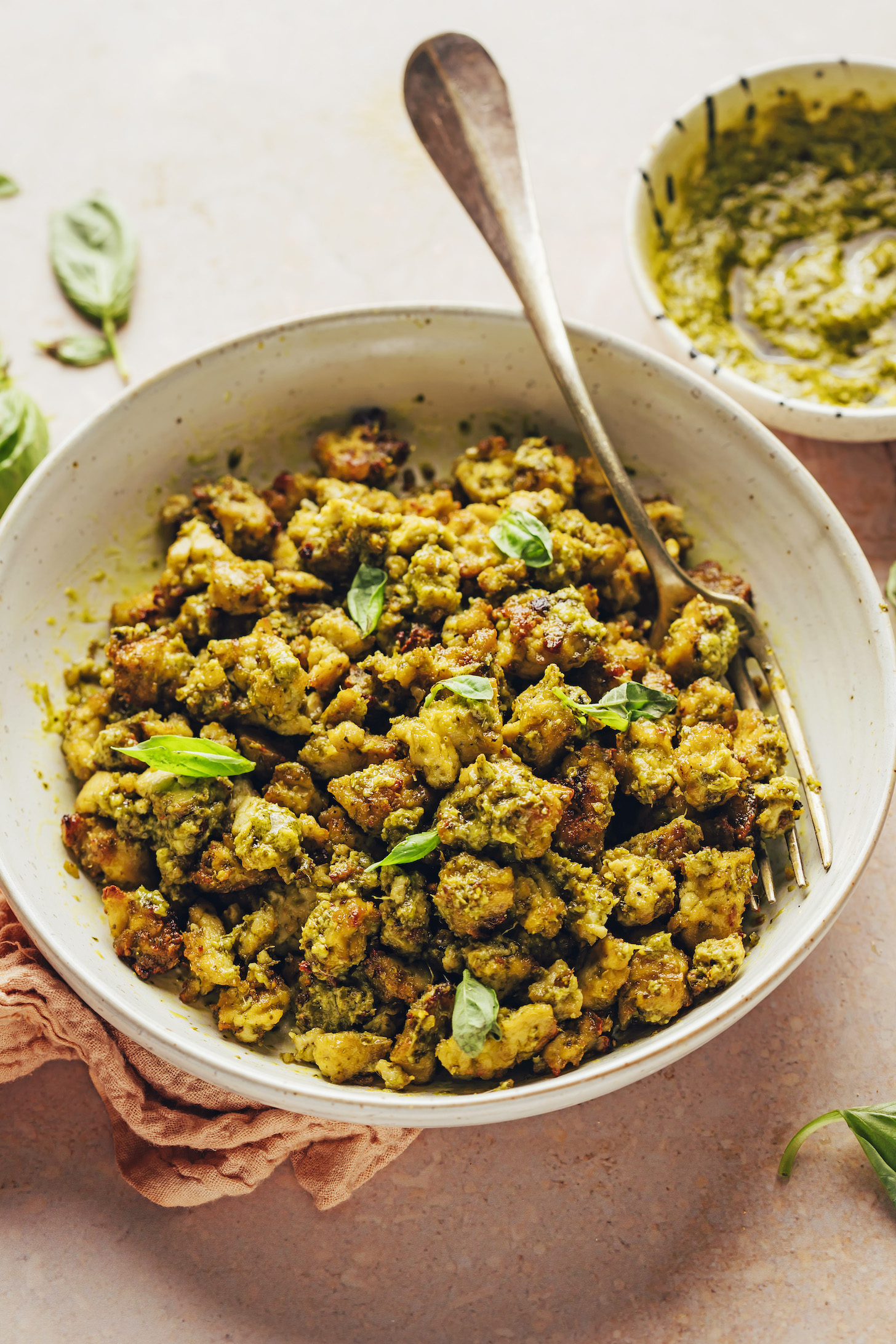 Crumbled crispy baked pesto tofu in a serving bowl topped with fresh basil leaves