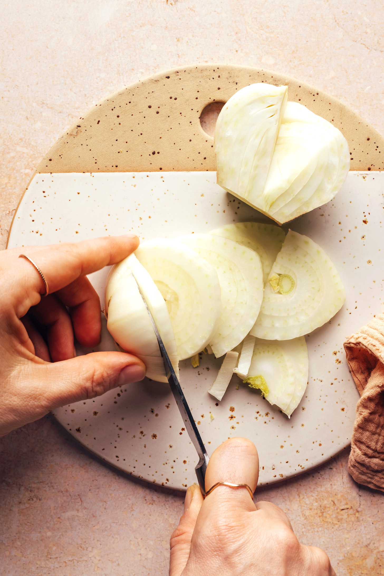 Using a knife to thinly slice a halved fennel bulb