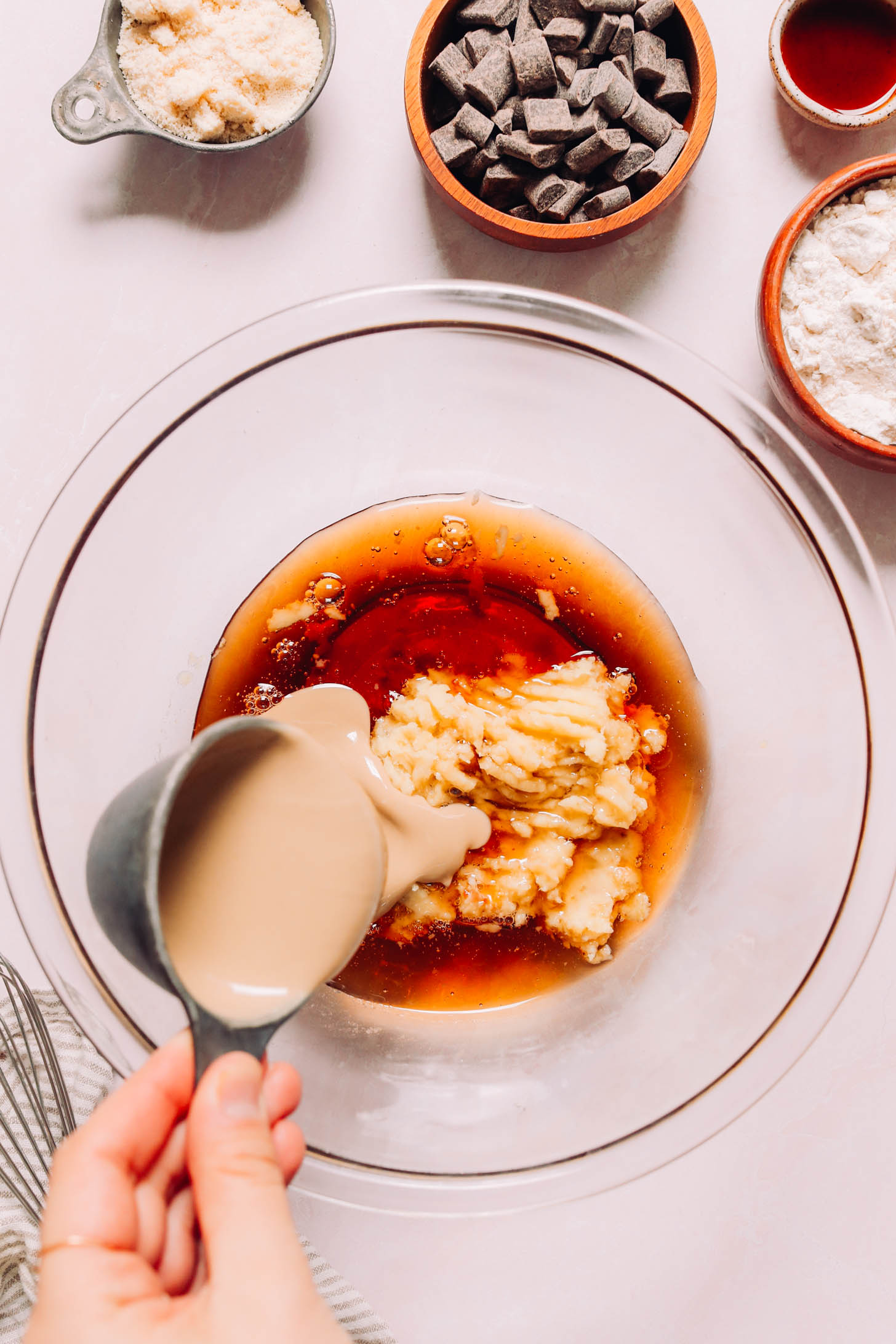 Pouring tahini into a bowl of maple syrup, sweet potato, and coconut oil