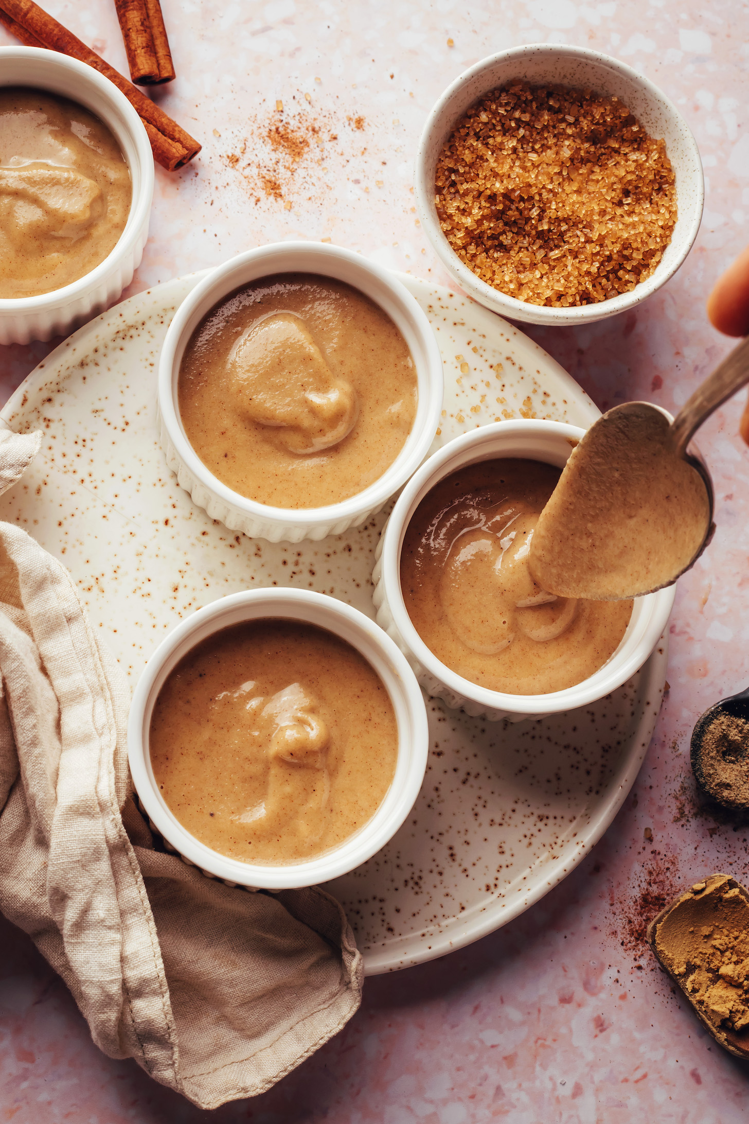 Using a spoon to transfer a creamy vegan chai-spiced custard into ramekins