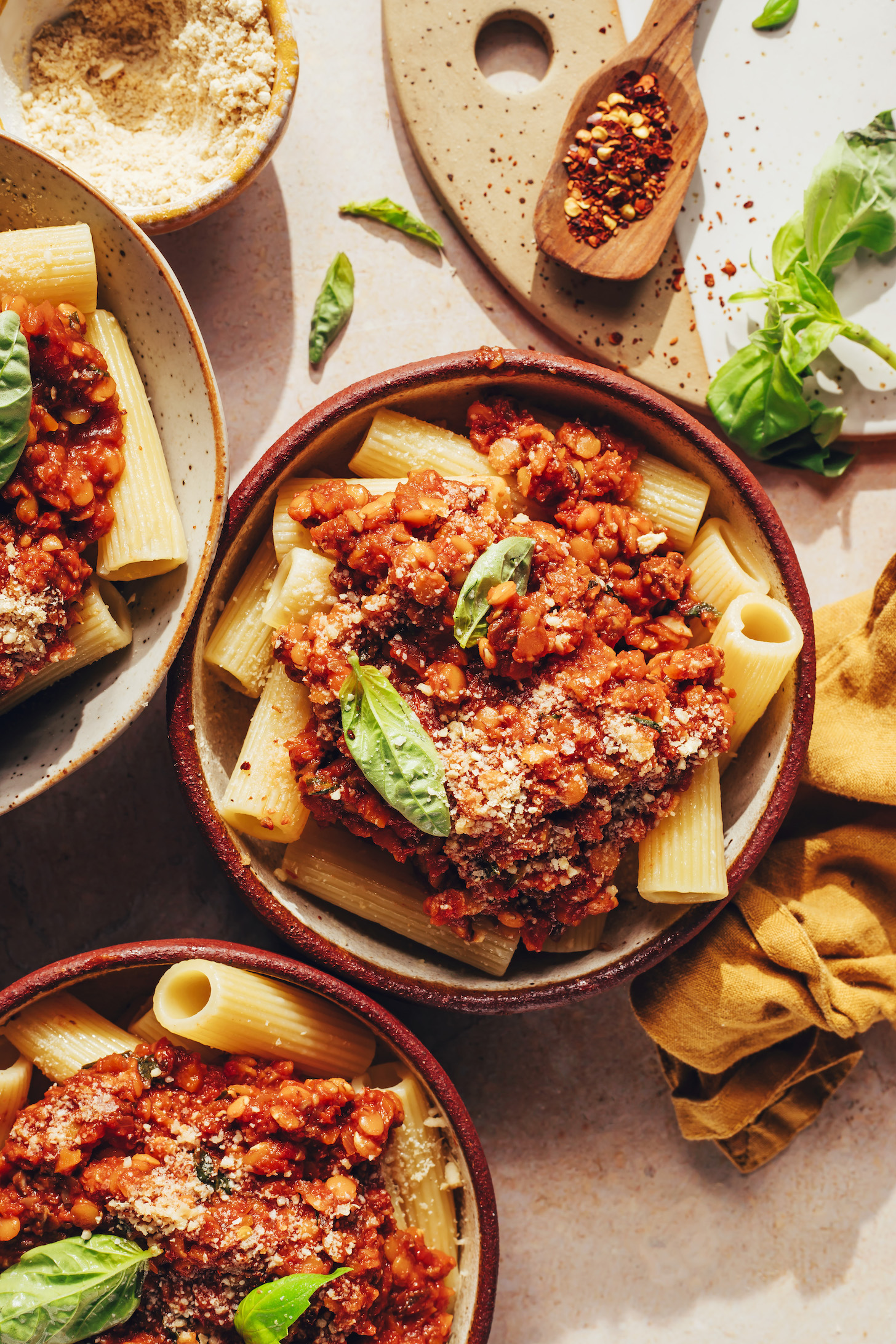 Bowls of pasta topped with vegan bolognese, basil, and vegan parmesan cheese