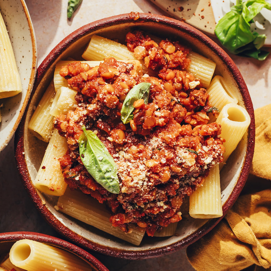 Close up shot of a bowl of vegan bolognese topped with basil and vegan parmesan cheese