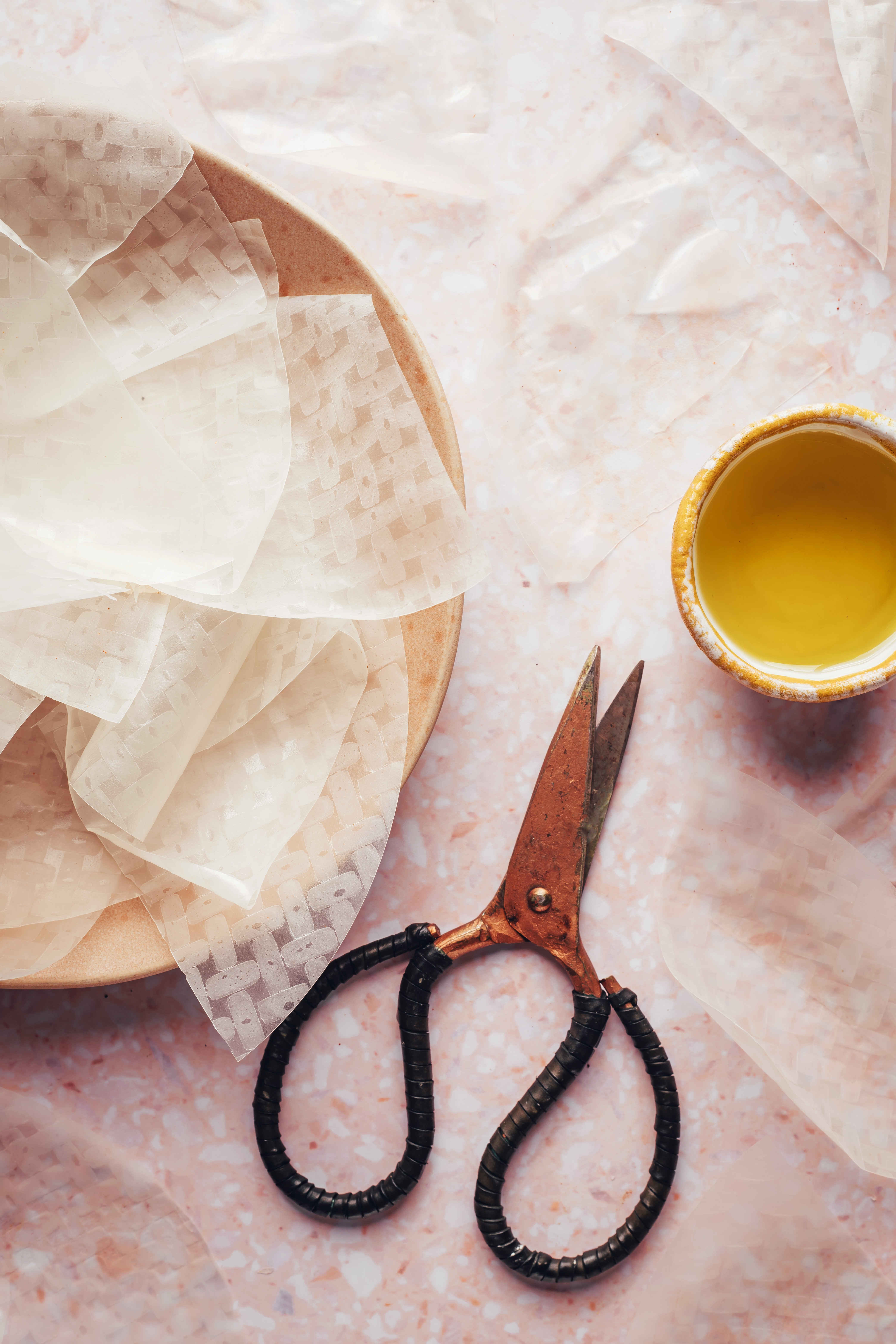 Scissors and oil next to a rice paper wrapper sliced into quarters