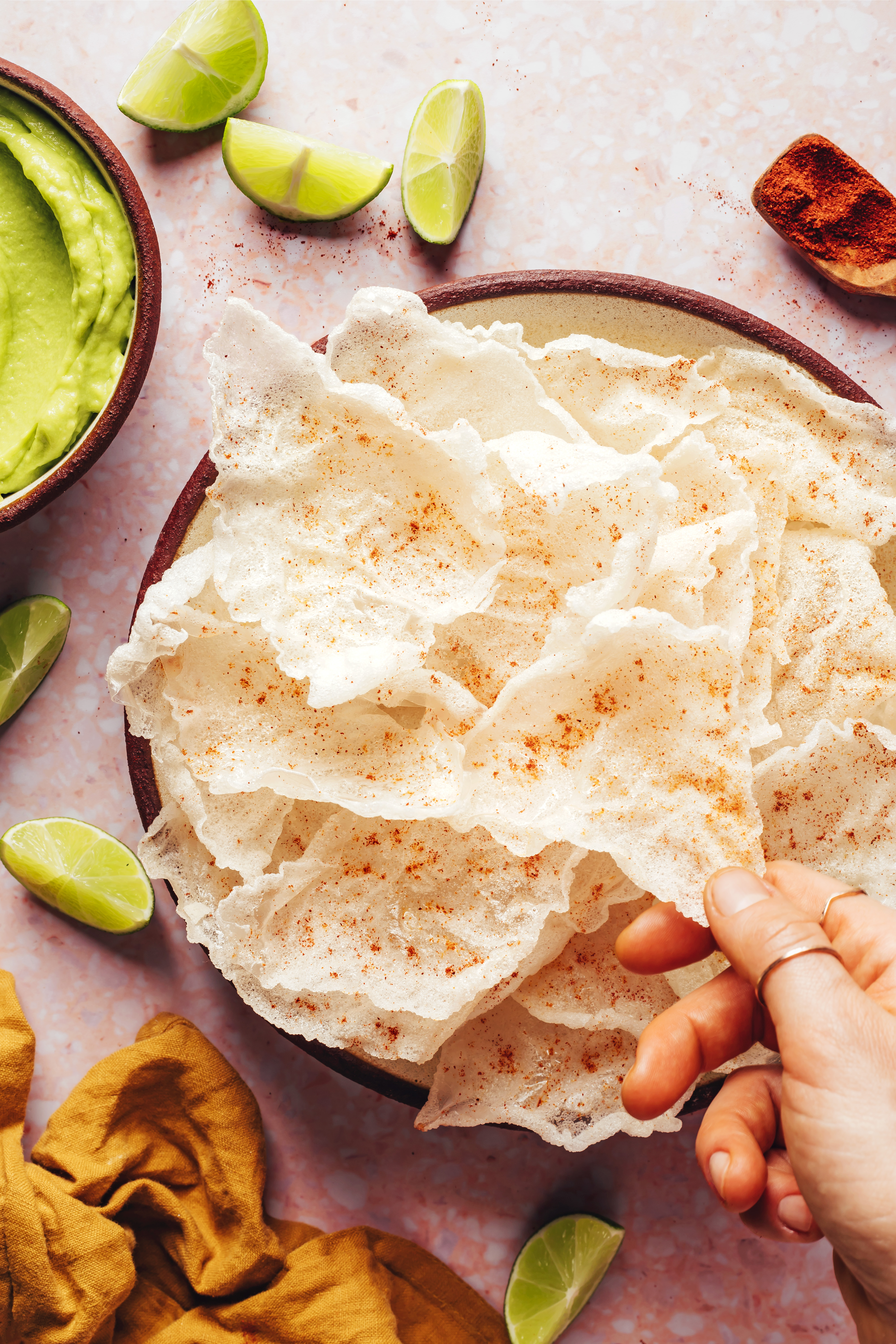 Fingers reaching in to grab a crispy rice paper chip from a plate