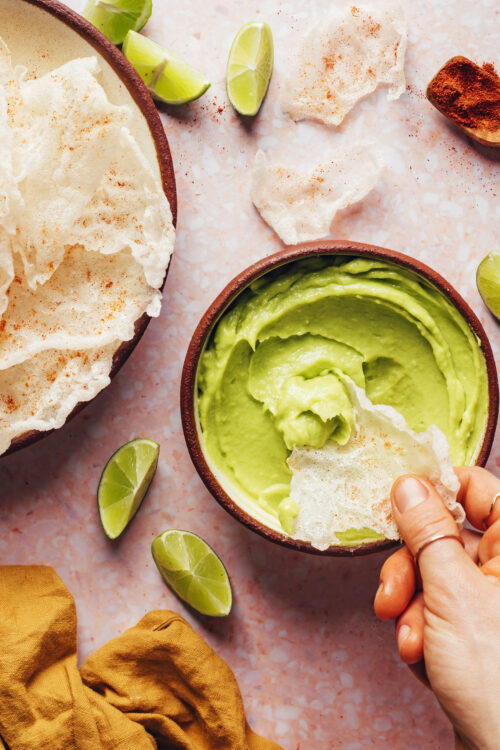 Dipping a crispy homemade rice paper chip into a bowl of vegan avocado dip