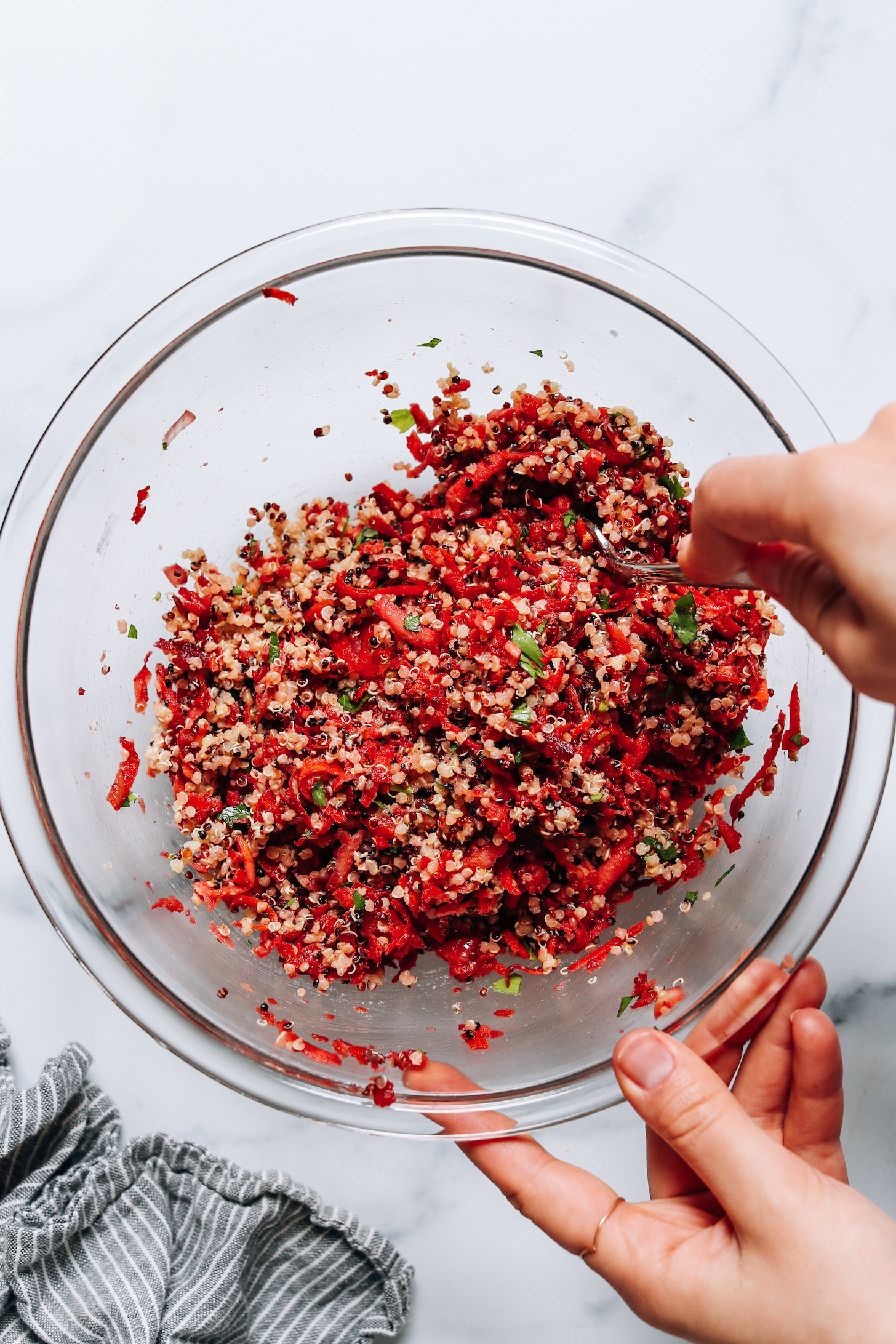 Using a spoon to mix sautéed root vegetables with quinoa and seasonings