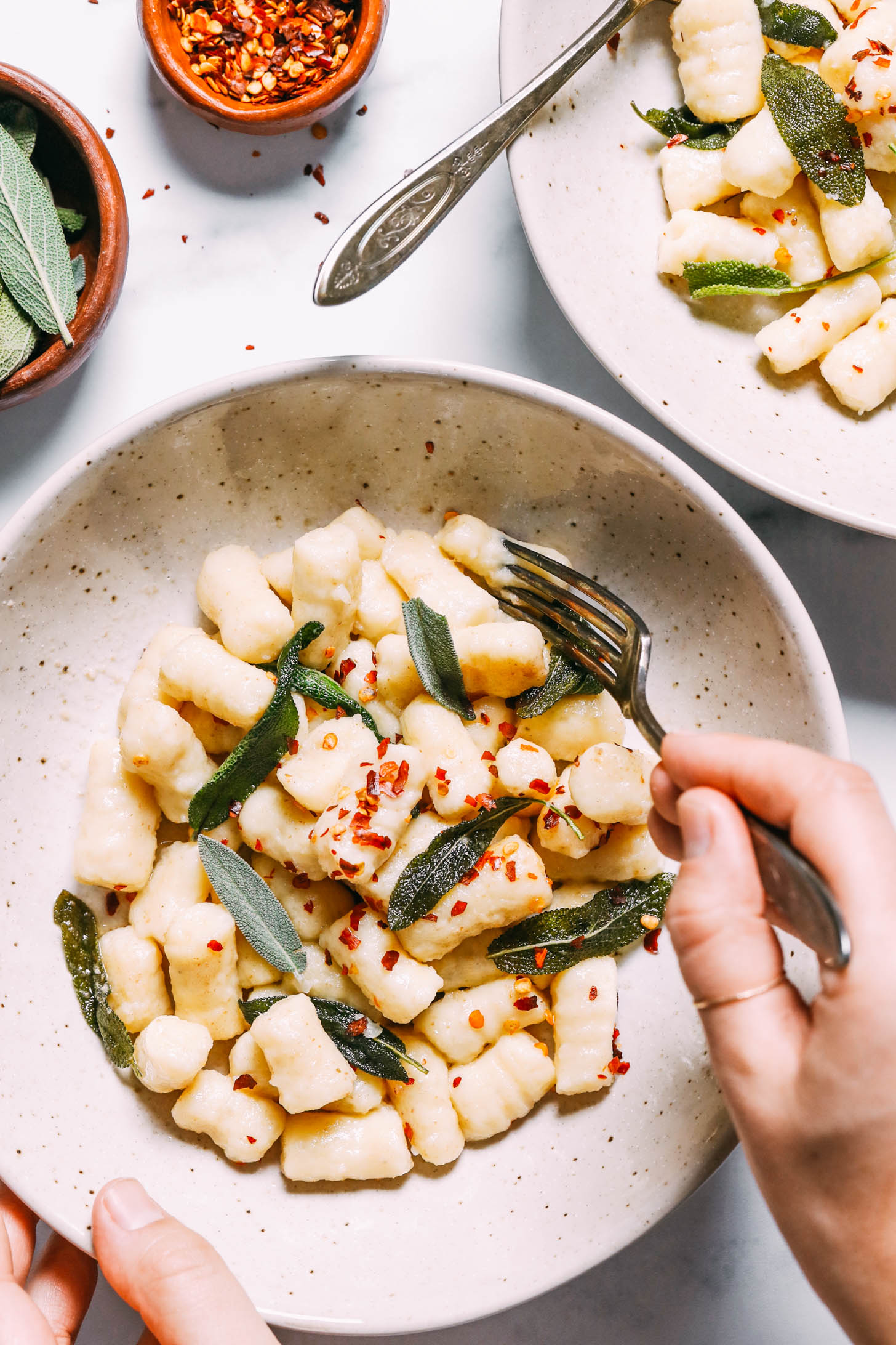 Gluten-free gnocchi plated with sage and red pepper flakes and being eaten with a fork
