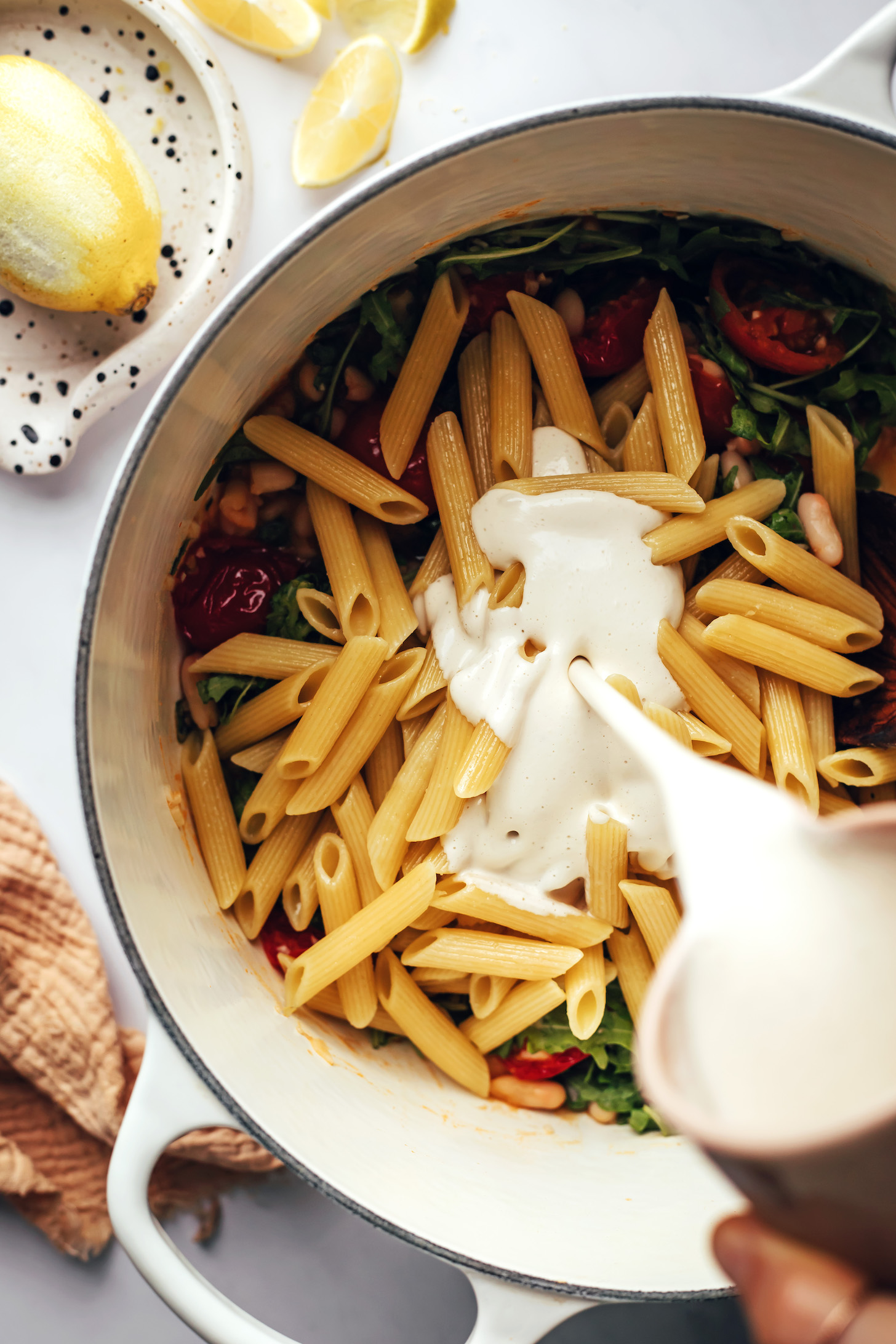 Pouring cashew sauce over pasta and veggies